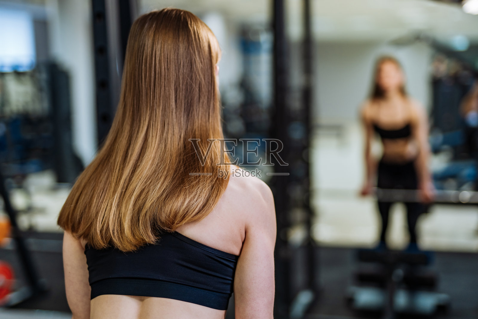 运动女性健美运动员在体育中心的镜子前做运动与模糊的背景。照片摄影图片