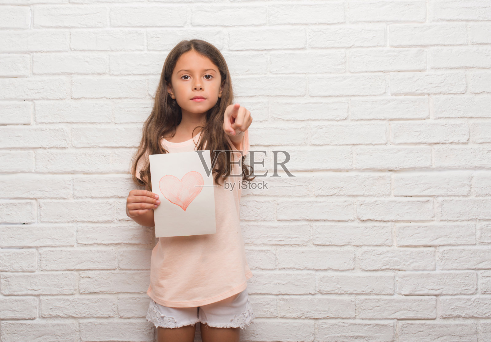 年轻的西班牙裔孩子在白色的砖墙上送着母亲节卡片，手指指着镜头和你，手势，正面积极而自信的手势照片摄影图片