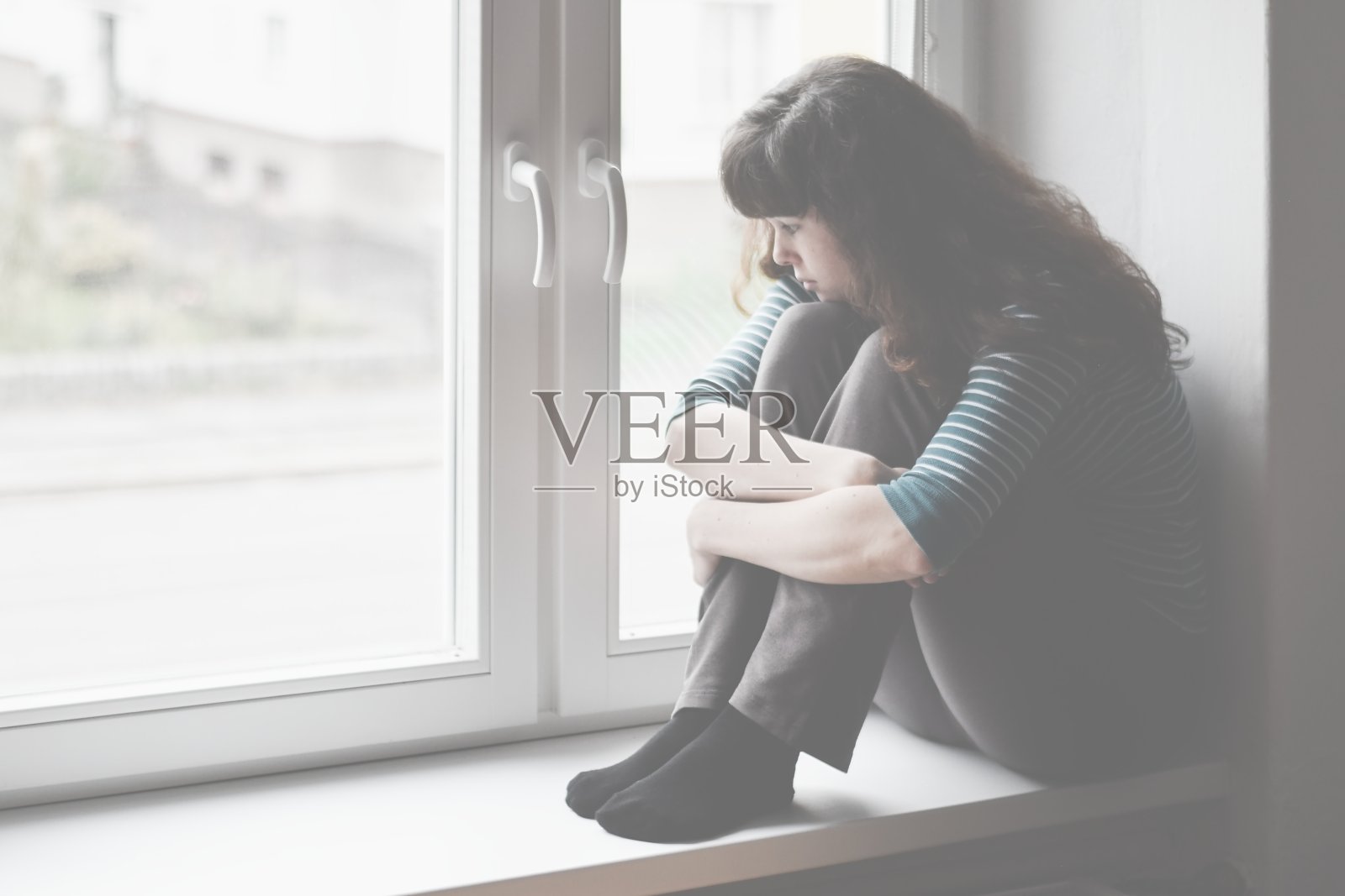 悲伤的年轻女子坐在窗边向外看照片摄影图片