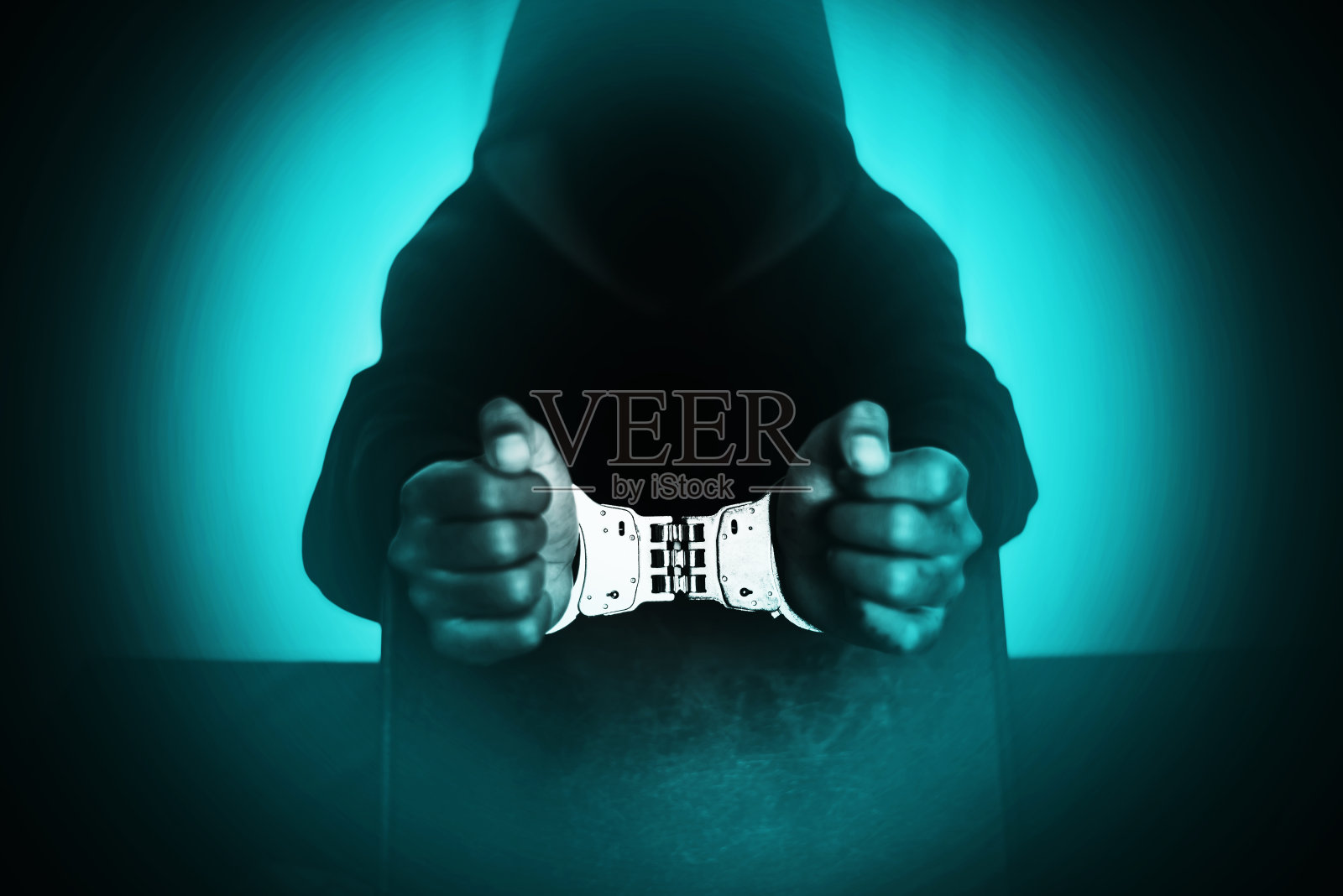 戴着手铐，戴着笔记本电脑，拿着钱，坐在办公桌前，这是网络犯罪的概念照片摄影图片