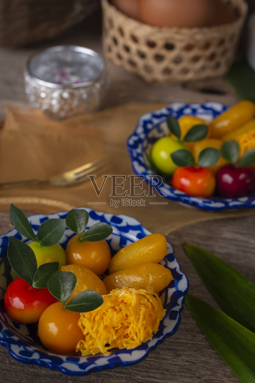 泰式甜点上有一盘白色和蓝色条纹的木桌上有类似的物体，叉子，香兰，椰子，鸡蛋在篮子里，水碗和金布周围放置。照片摄影图片