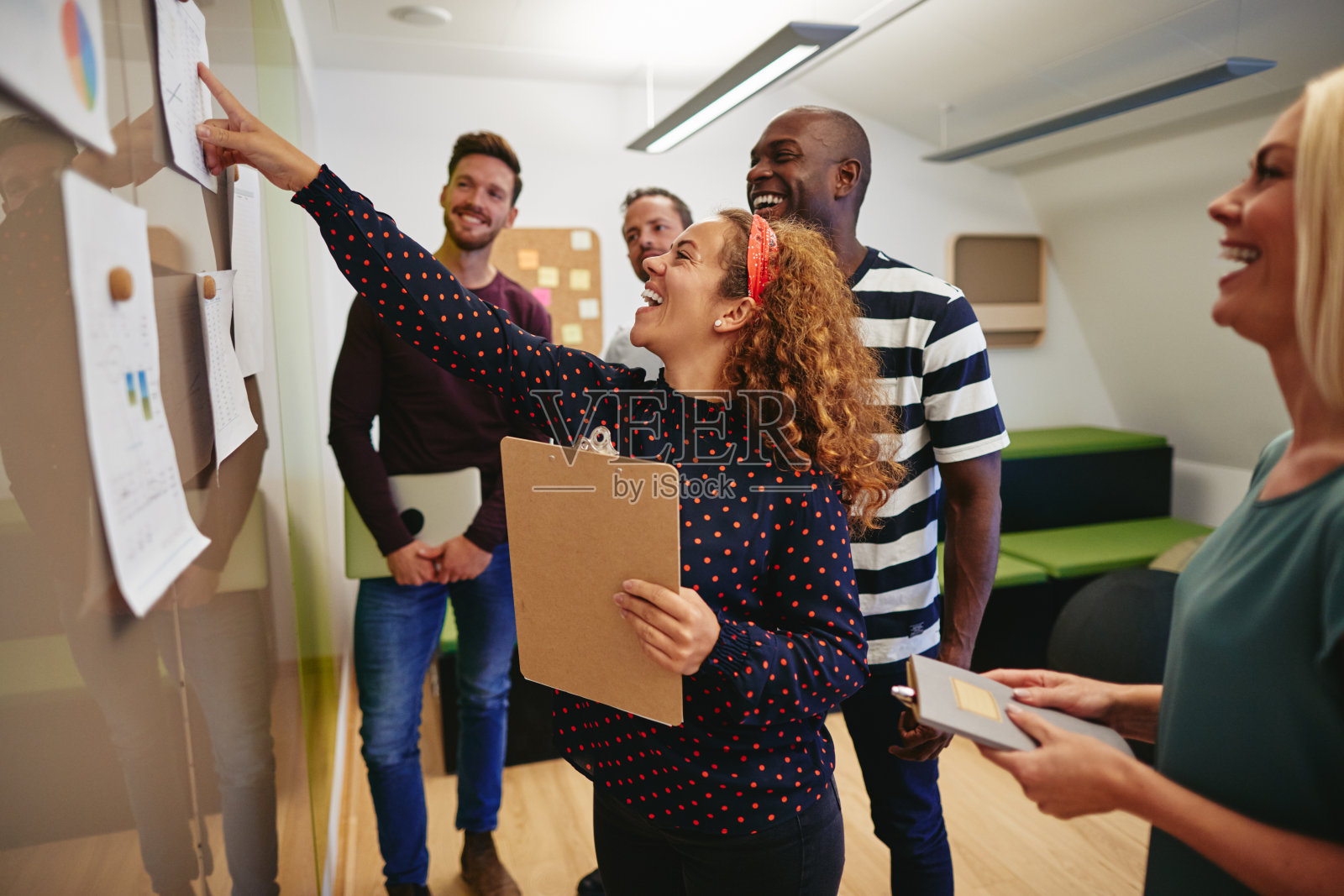 同事们微笑着看挂在办公室墙上的文件照片摄影图片