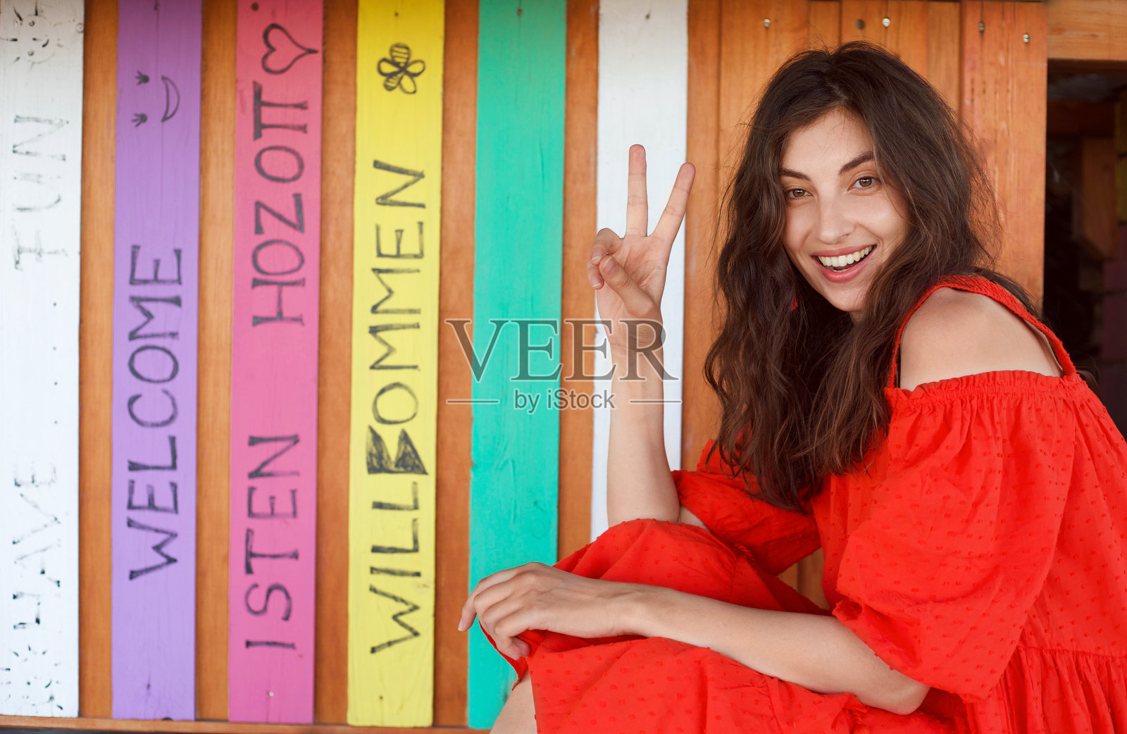 漂亮的女孩穿着红色的夏装，旁边是一堵彩色的墙壁，上面写着欢迎的话。照片摄影图片