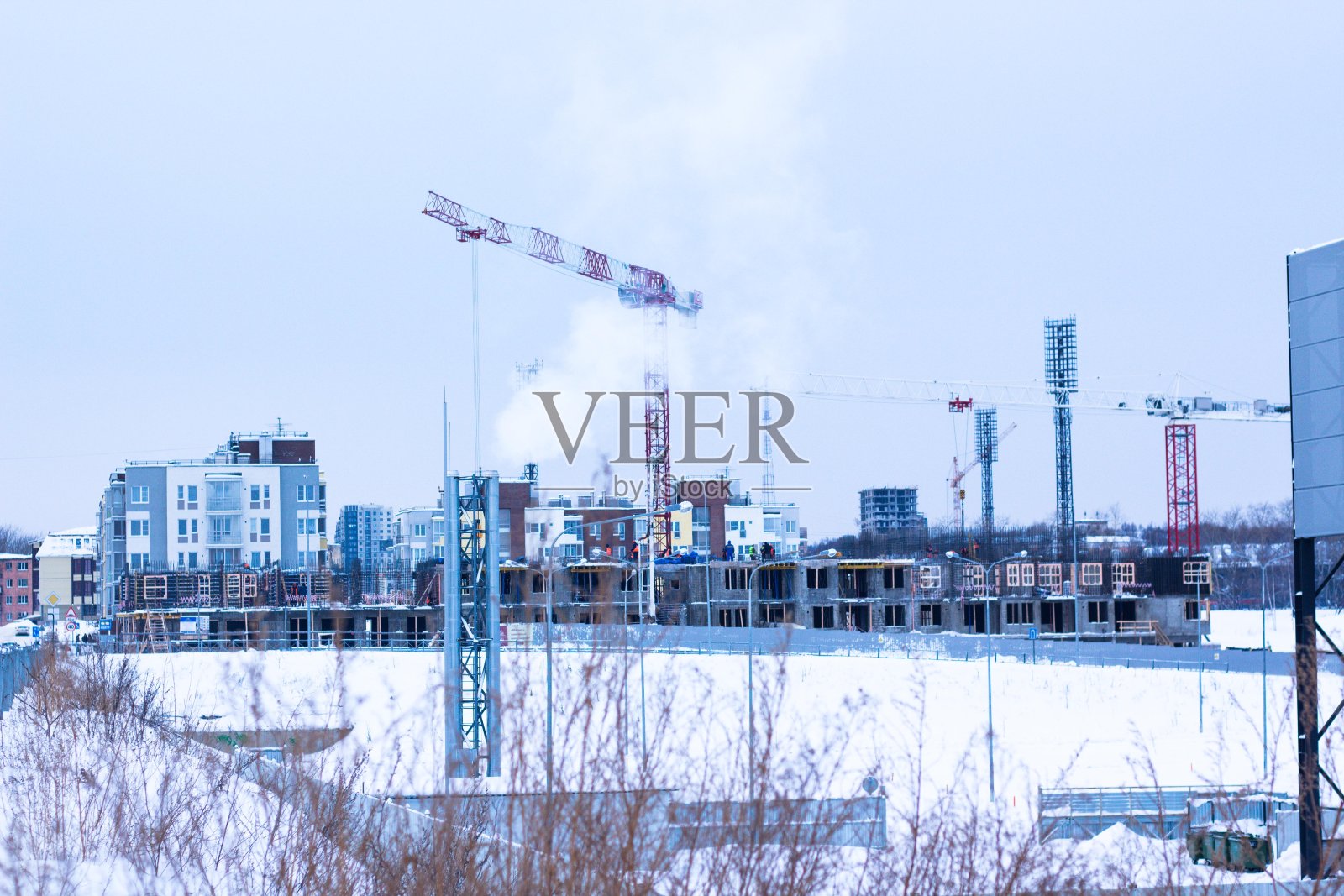 在正在建设的房屋的背景下，烟从烟囱的管道中高高地升起。本世纪的房屋建筑业每天都在快速发展。照片摄影图片