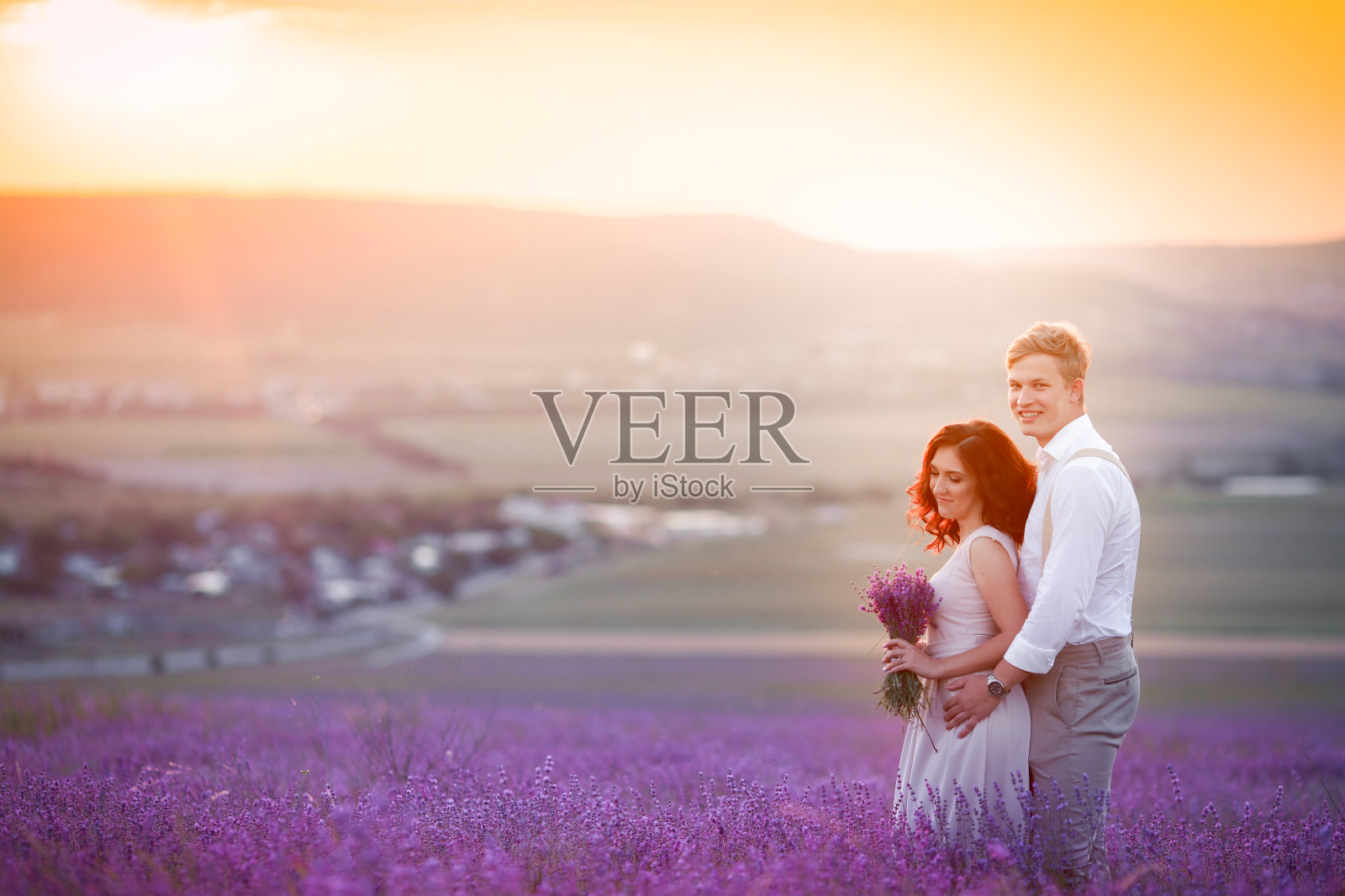 年轻的情侣在热恋中的新郎和新娘，婚礼的日子在夏天。在薰衣草地里享受幸福和爱的时刻。穿着豪华婚纱的新娘。照片摄影图片