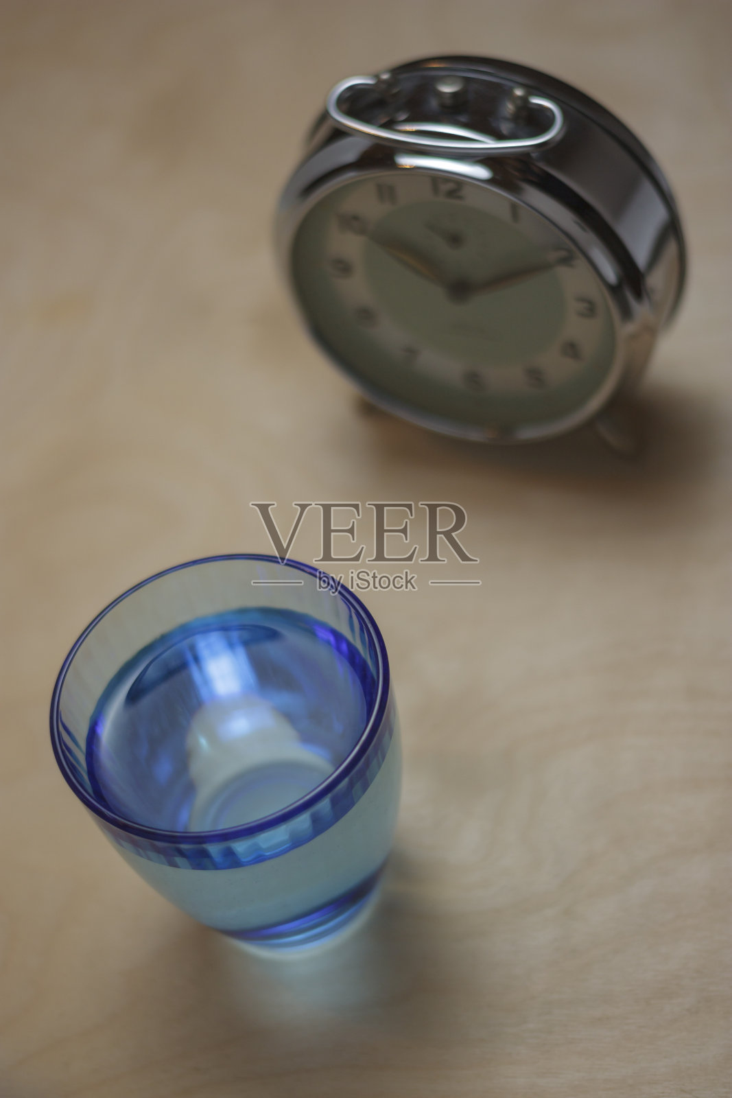 木桌上放着一杯水，背景是一个时钟照片摄影图片