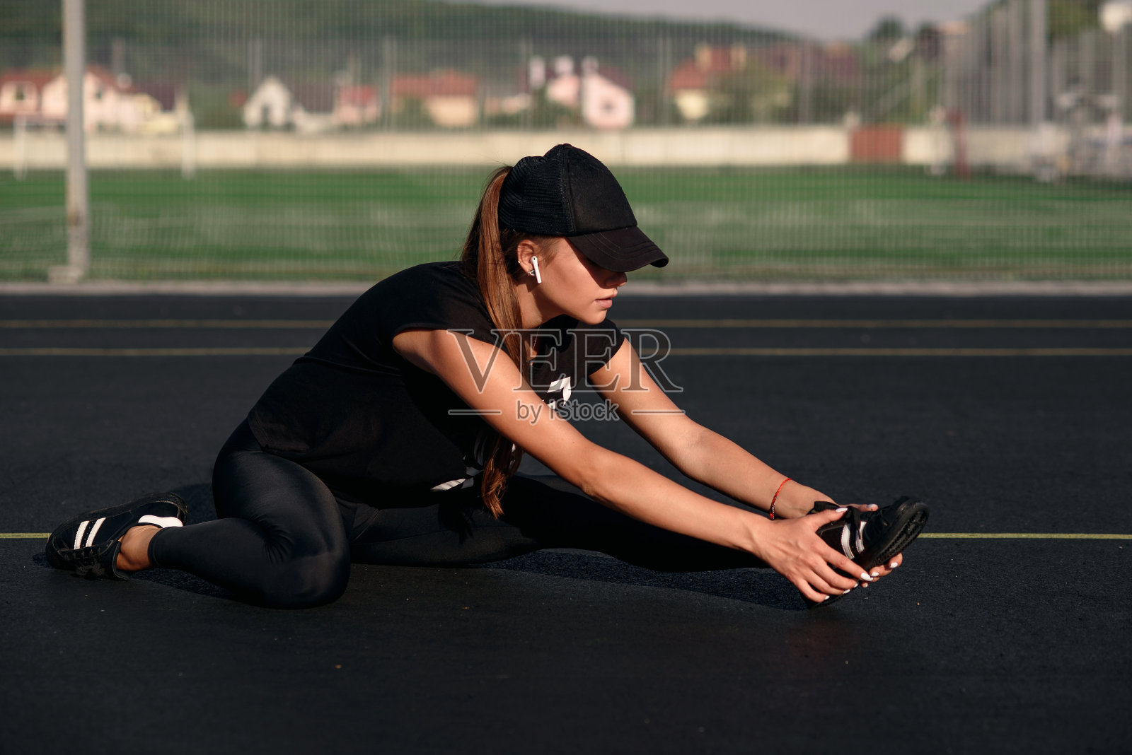 一个漂亮的女孩穿着黑色运动服，戴着黑色的帽子，在训练前在网球场做热身运动。照片摄影图片