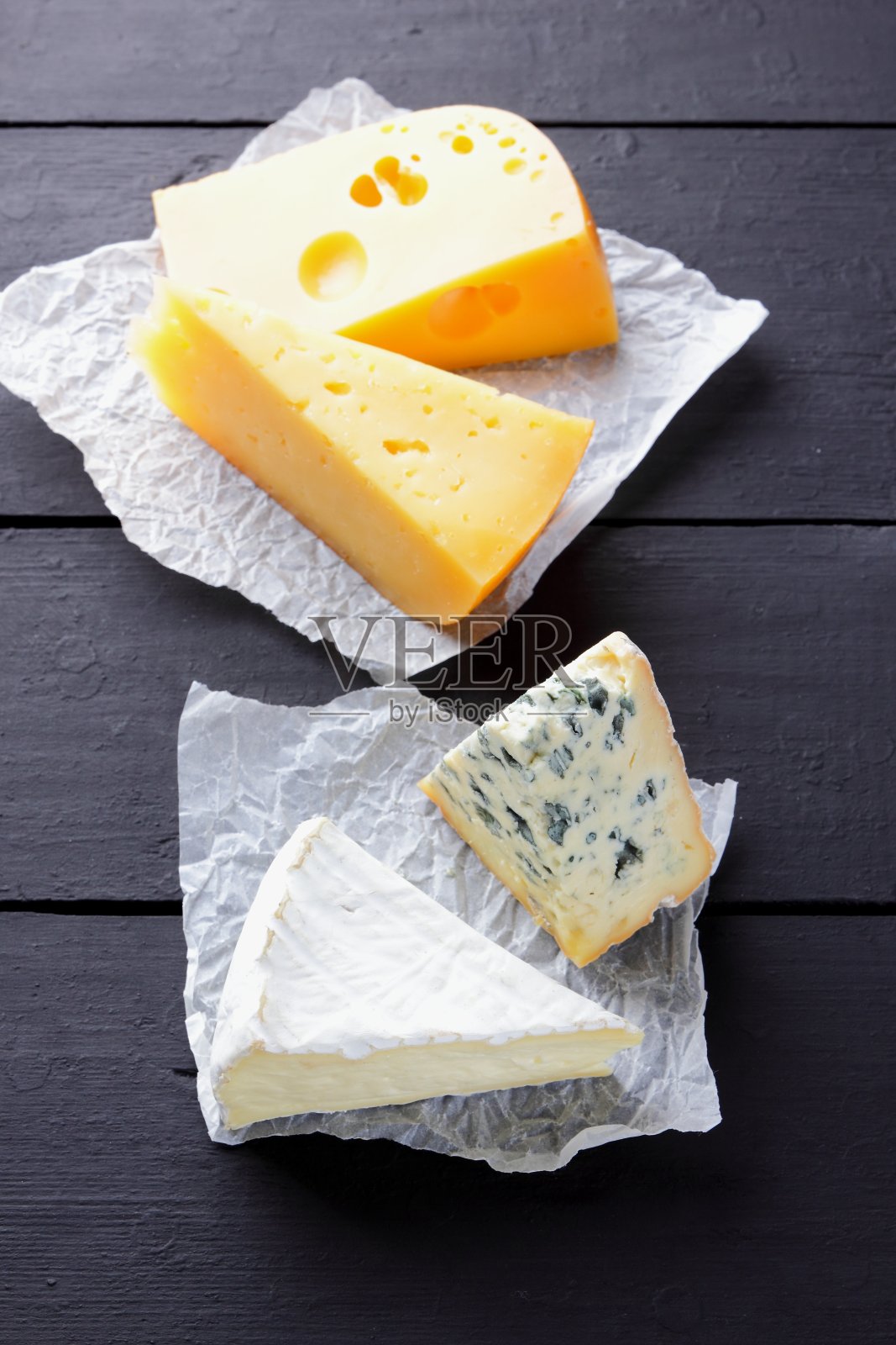 黑色的黑板上有坚硬的黄色奶酪、卡门贝尔奶酪和蓝色奶酪。各种各样的奶酪放在羊皮纸上。瑞士奶酪和dorblu的深色背景。俯视图照片摄影图片