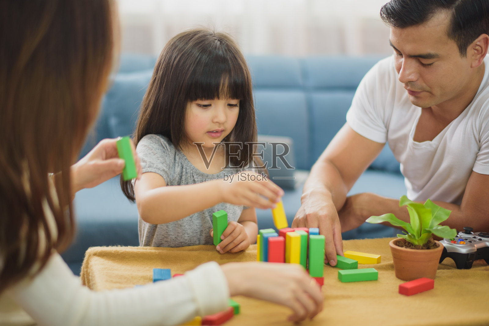 家庭时间女儿笑着和父母在家里沙发前的桌子上玩耍。照片摄影图片