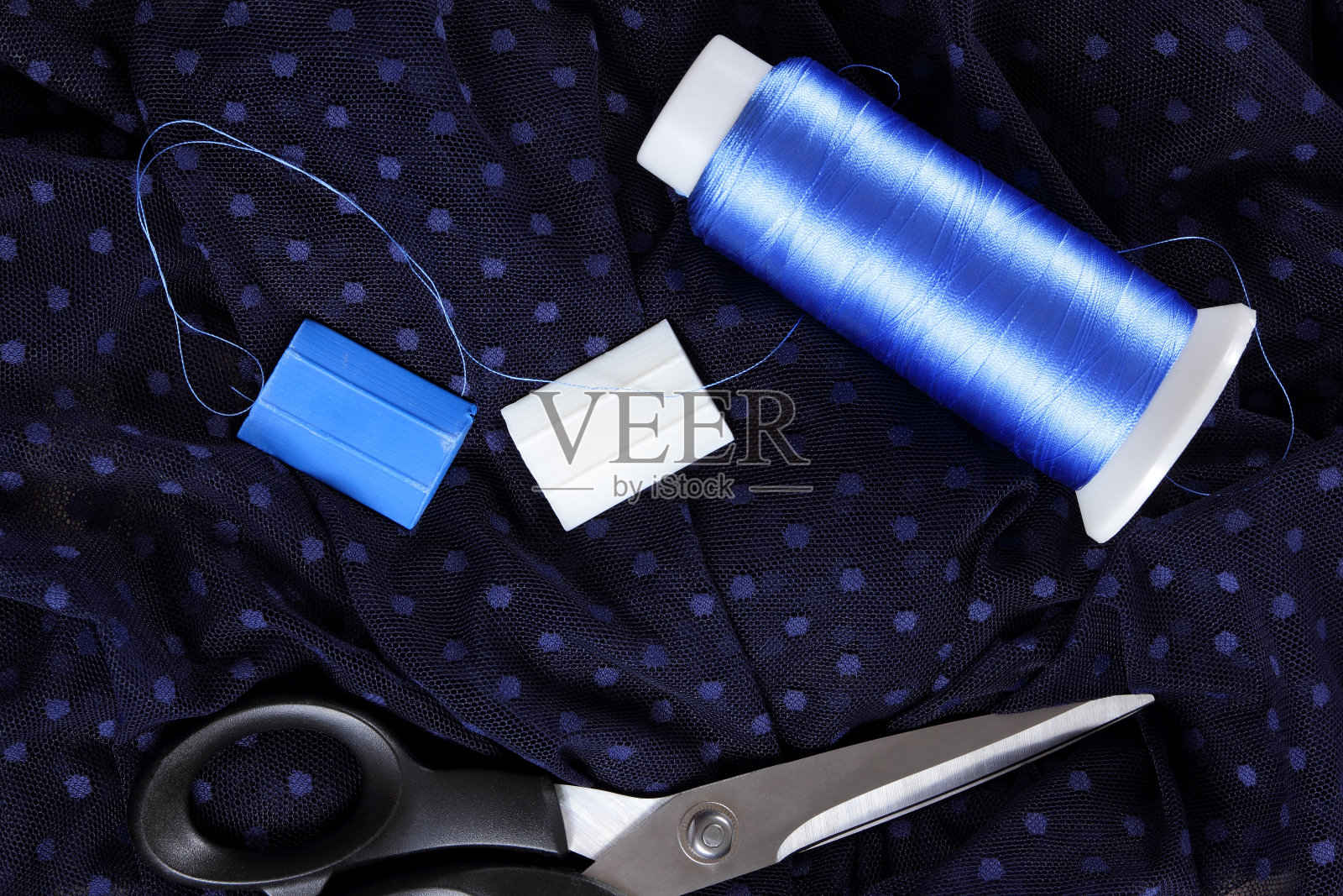 深色布，有圆点和蓝色丝线。裁剪的过程。黑色织物上的剪刀和线轴。用于缝纫的亮蓝色线。俯视图照片摄影图片