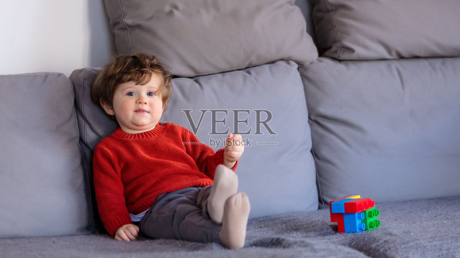 滑稽的小男孩穿着红毛衣坐在沙发上照片摄影图片