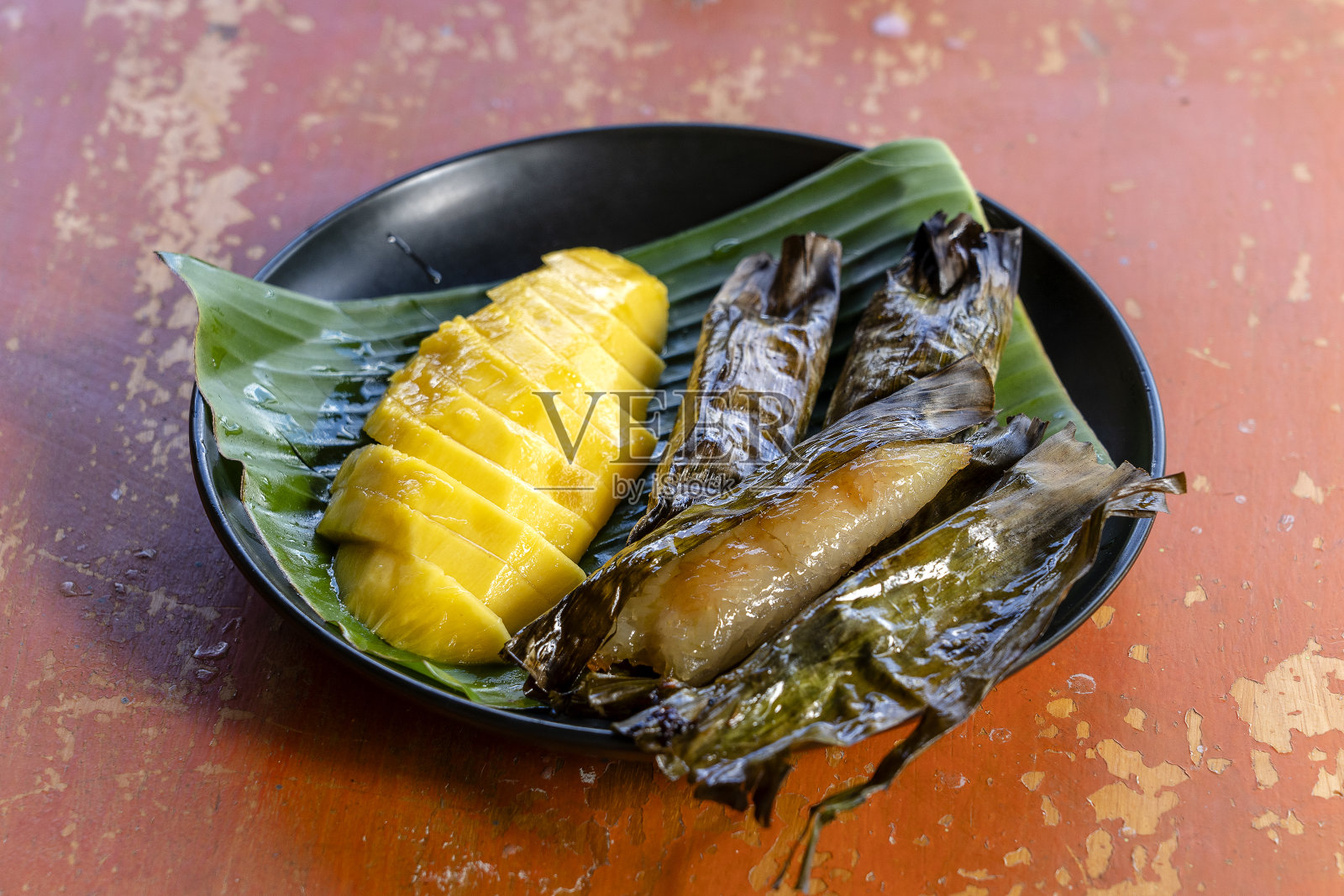 泰式甜点，黄芒果和香蕉糯米在棕榈叶。黄芒果和糯米是泰国受欢迎的传统甜点。照片摄影图片