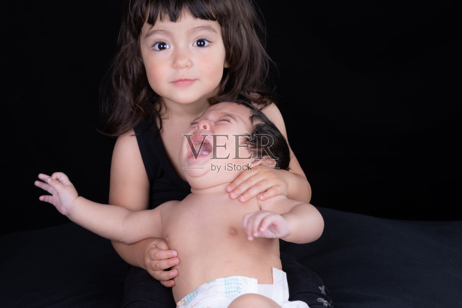 摄影棚拍摄到一个蹒跚学步的小女孩抱着她哭泣的小弟弟照片摄影图片