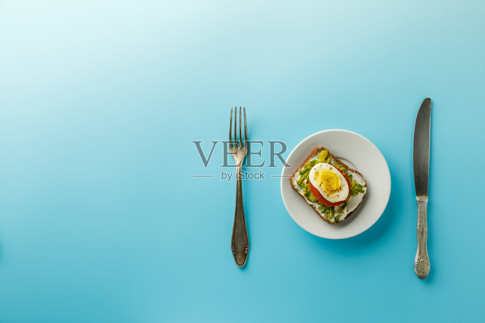 蓝色背景的白色盘子上有鸡蛋和鳄梨三明治，俯视图照片摄影图片