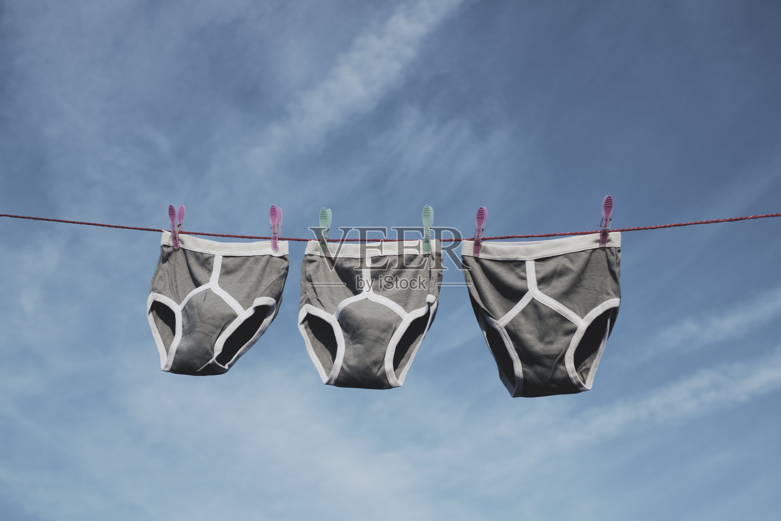 蓝天下，晾衣绳上挂着三条灰色复古Y-Front内裤。照片摄影图片