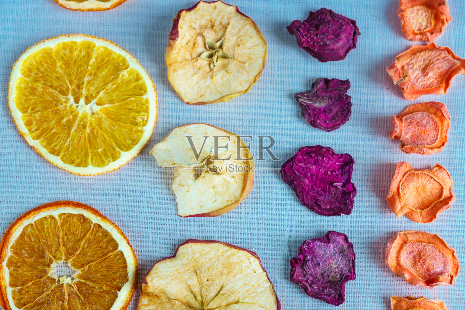 健康食品有机营养。将苹果、橘子、胡萝卜、甜菜切片、干片排成一行，铺在纺织品的背景上。照片摄影图片