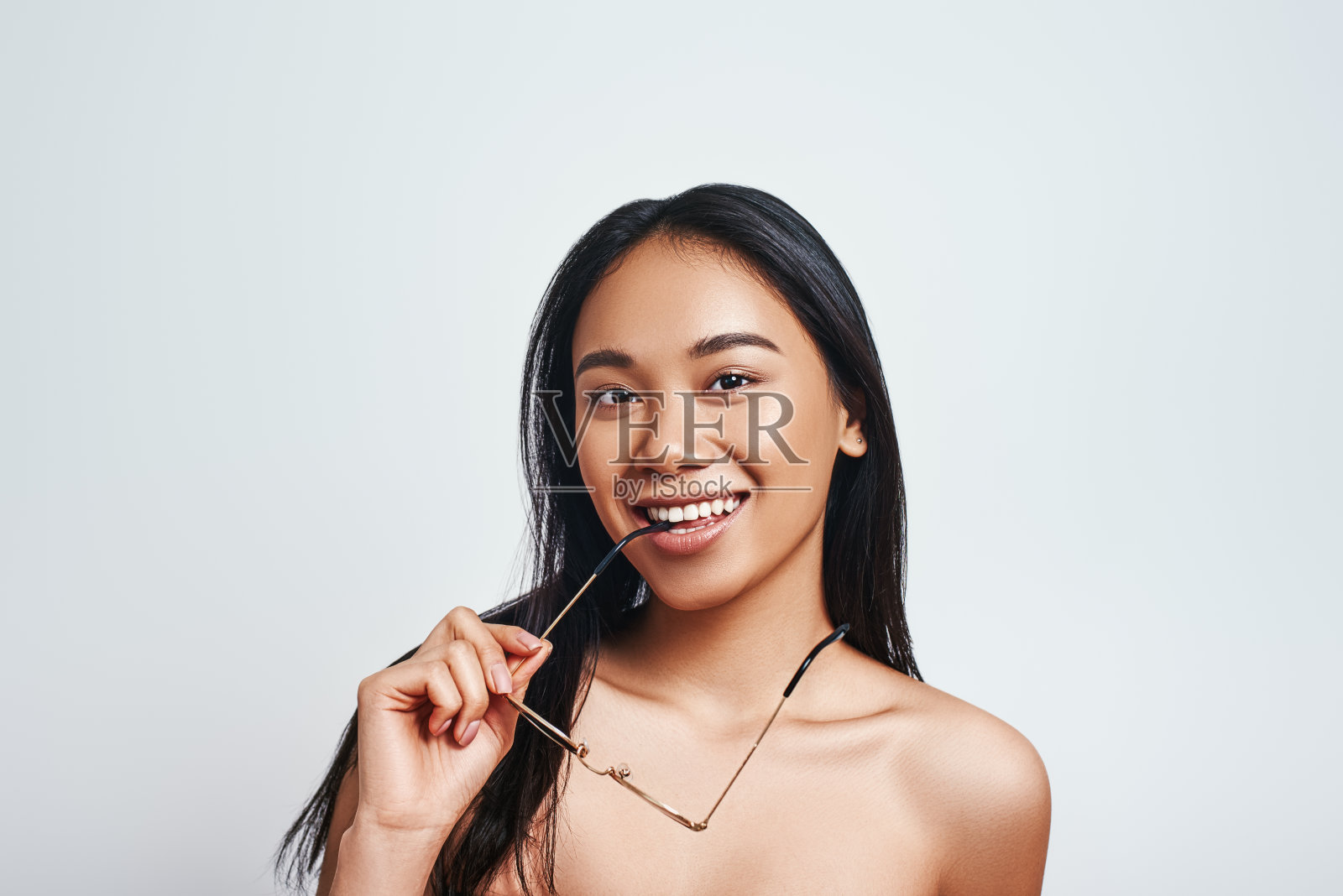 纯粹的美。漂亮的年轻亚洲女人脱下她的太阳镜和微笑，而站在白色的背景。美丽的概念照片摄影图片