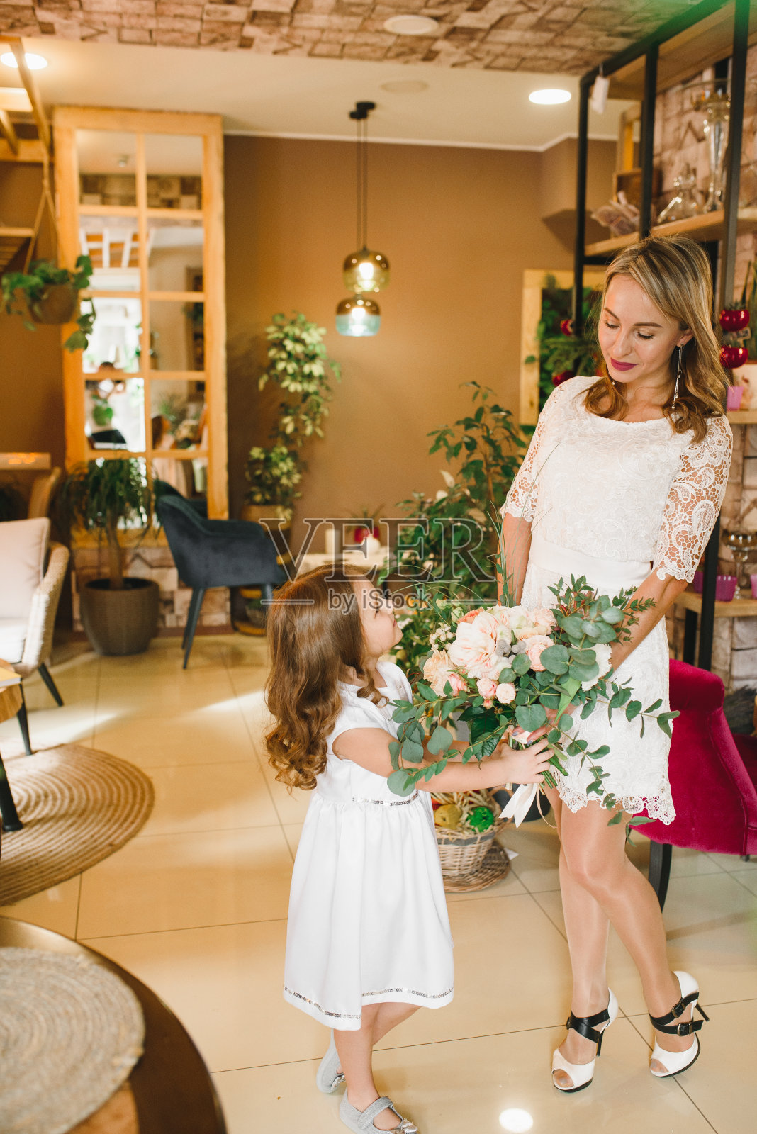 妈妈和女儿带着花在咖啡厅。儿子送花给妈妈。可爱的家庭。国际妇女节，3月8日庆祝照片摄影图片