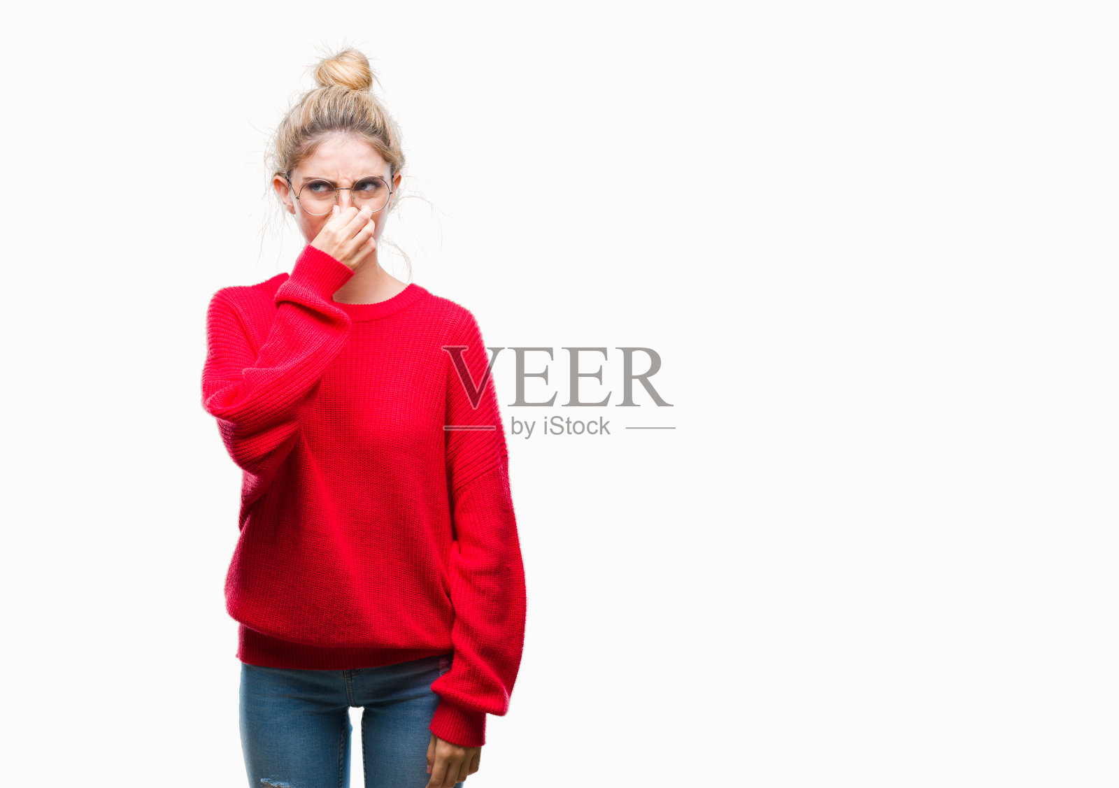 年轻美丽的金发女人穿着红色的毛衣和眼镜在孤立的背景闻一些恶臭和恶心，难以忍受的气味，屏住呼吸用手指在鼻子上。“坏味道”的概念。照片摄影图片