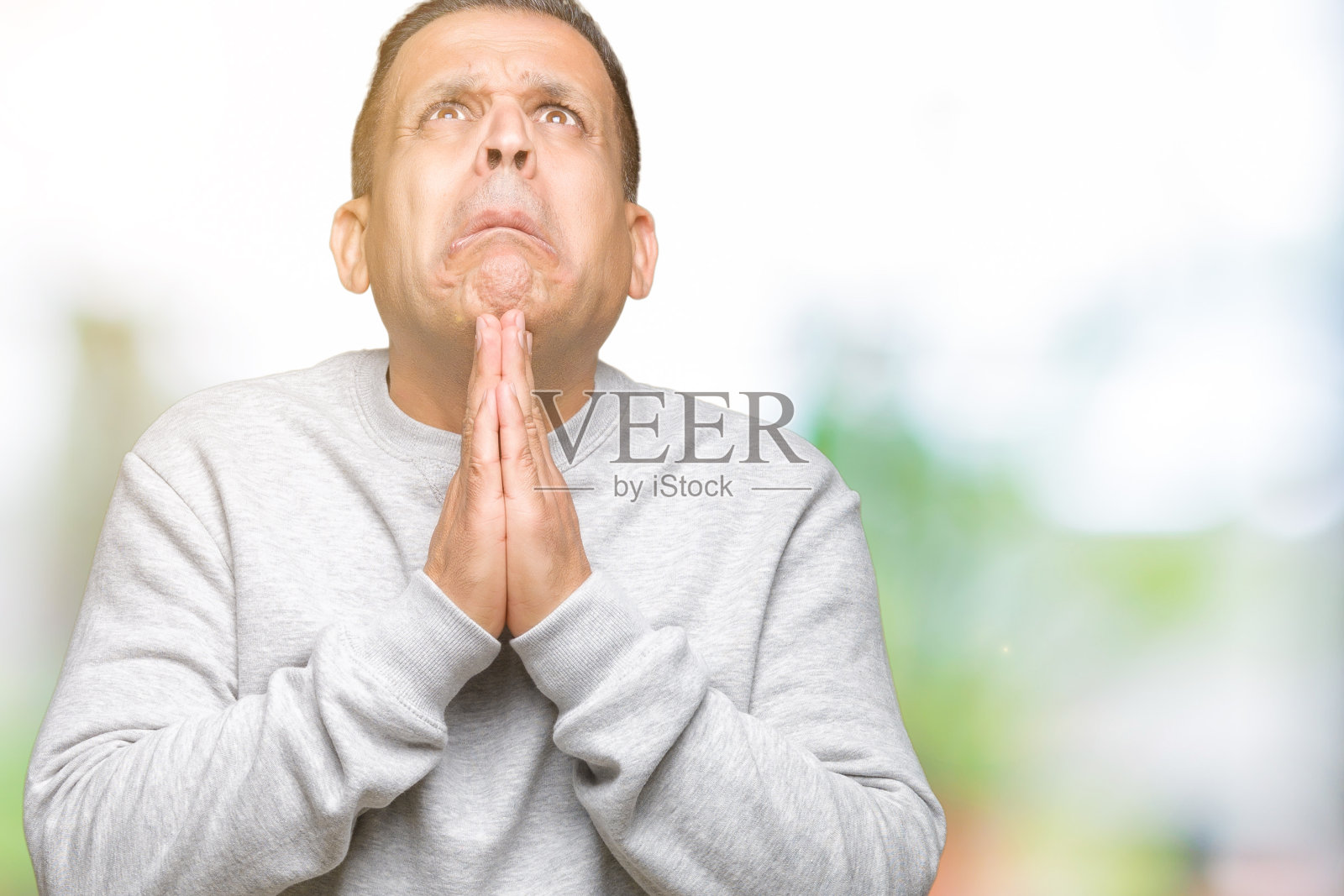 孤立背景下穿着运动衫，双手合十祈祷的中年阿拉伯男人照片摄影图片