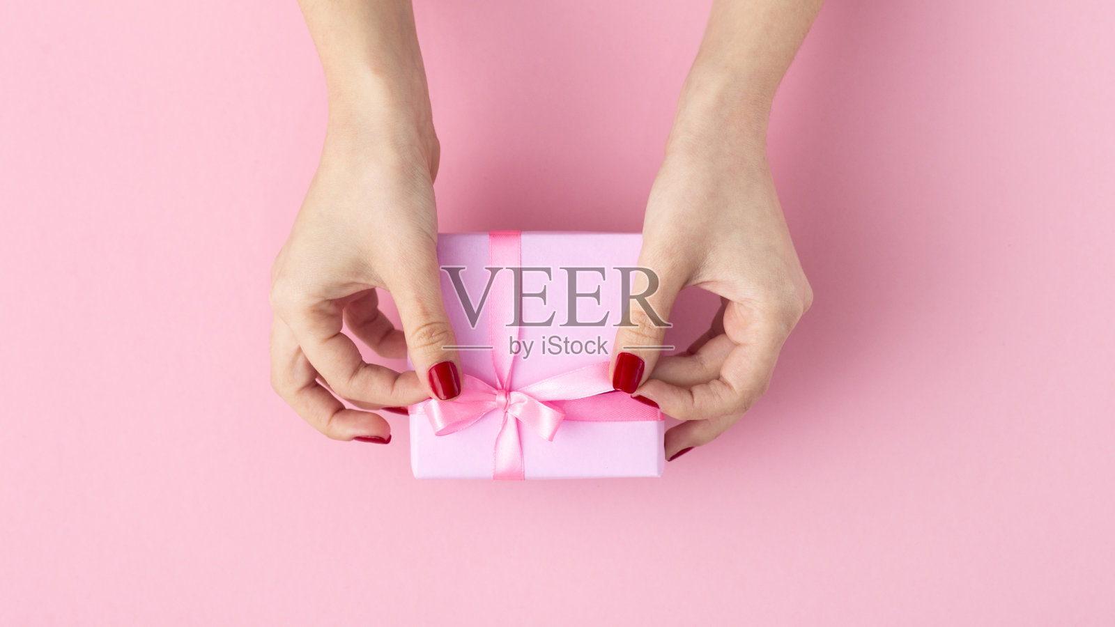 女孩手里拿着礼物，女人的手打开盒子包装在装饰纸上粉色的背景，俯视图，概念节日和礼物照片摄影图片