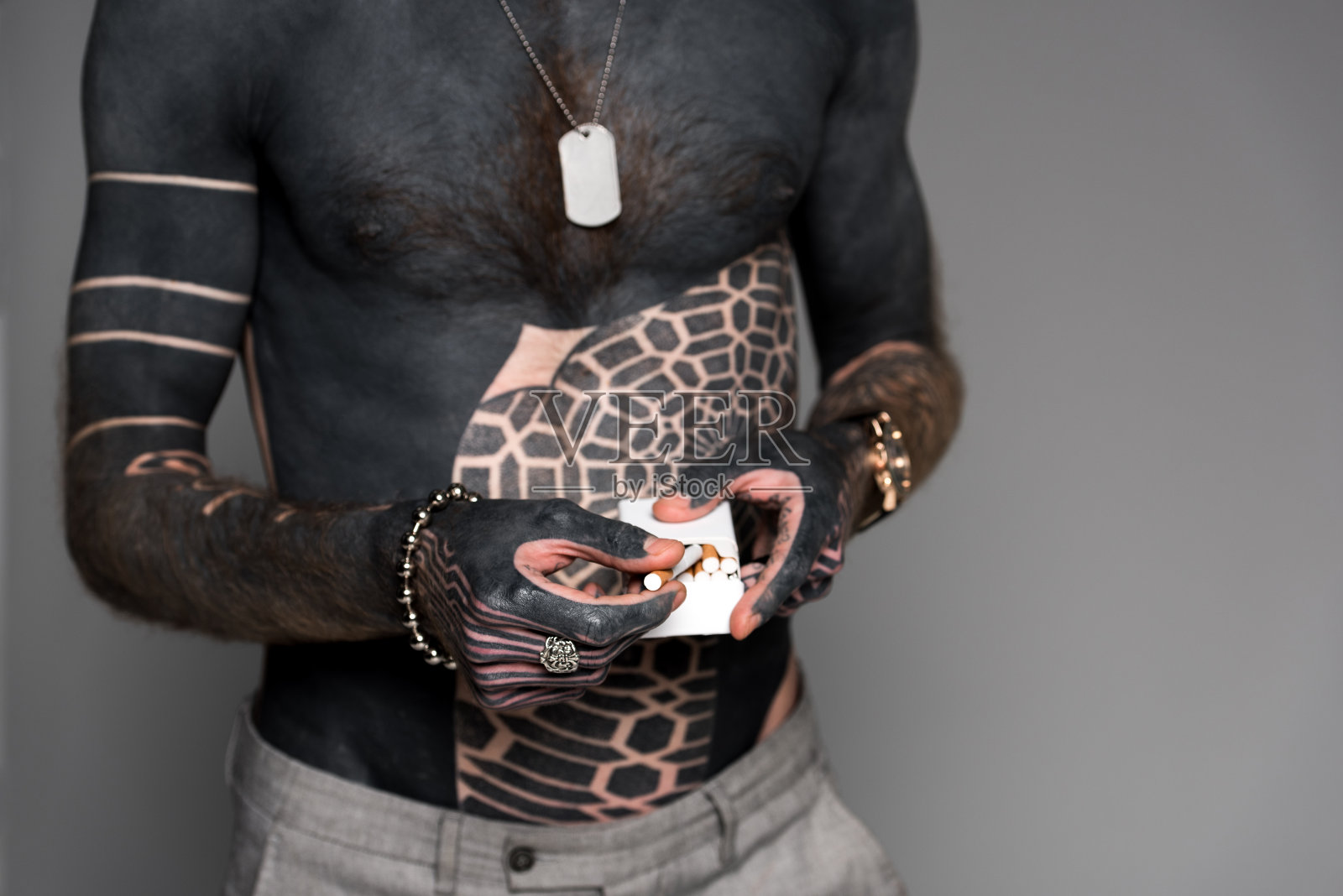 中间部分赤裸上身的男子与纹身拿着烟盒孤立在灰色照片摄影图片