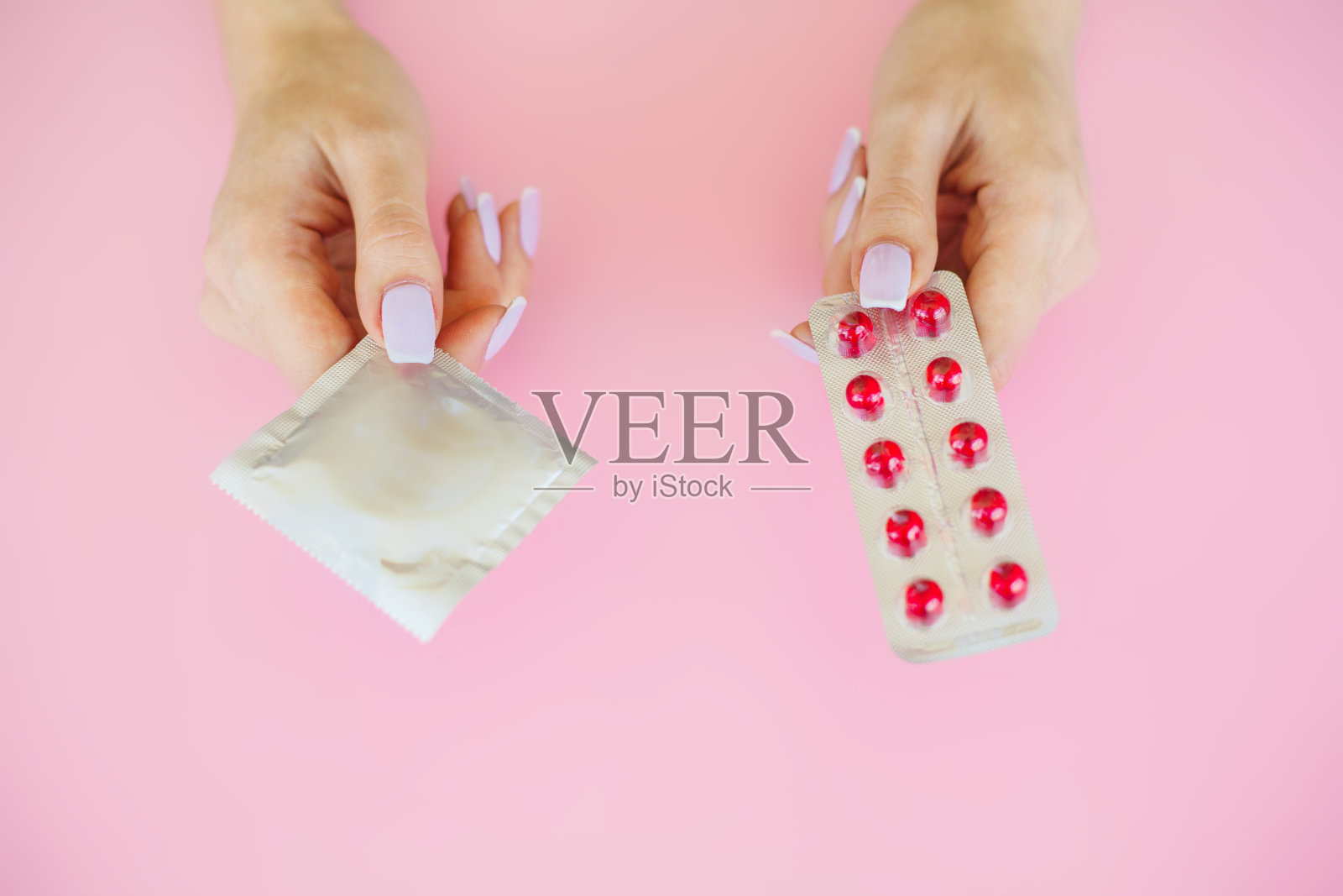 避孕。避孕药和一个打开的避孕套。粉红色背景上的彩色药丸和胶囊。药房主题，胶囊药丸与药物抗生素包装照片摄影图片