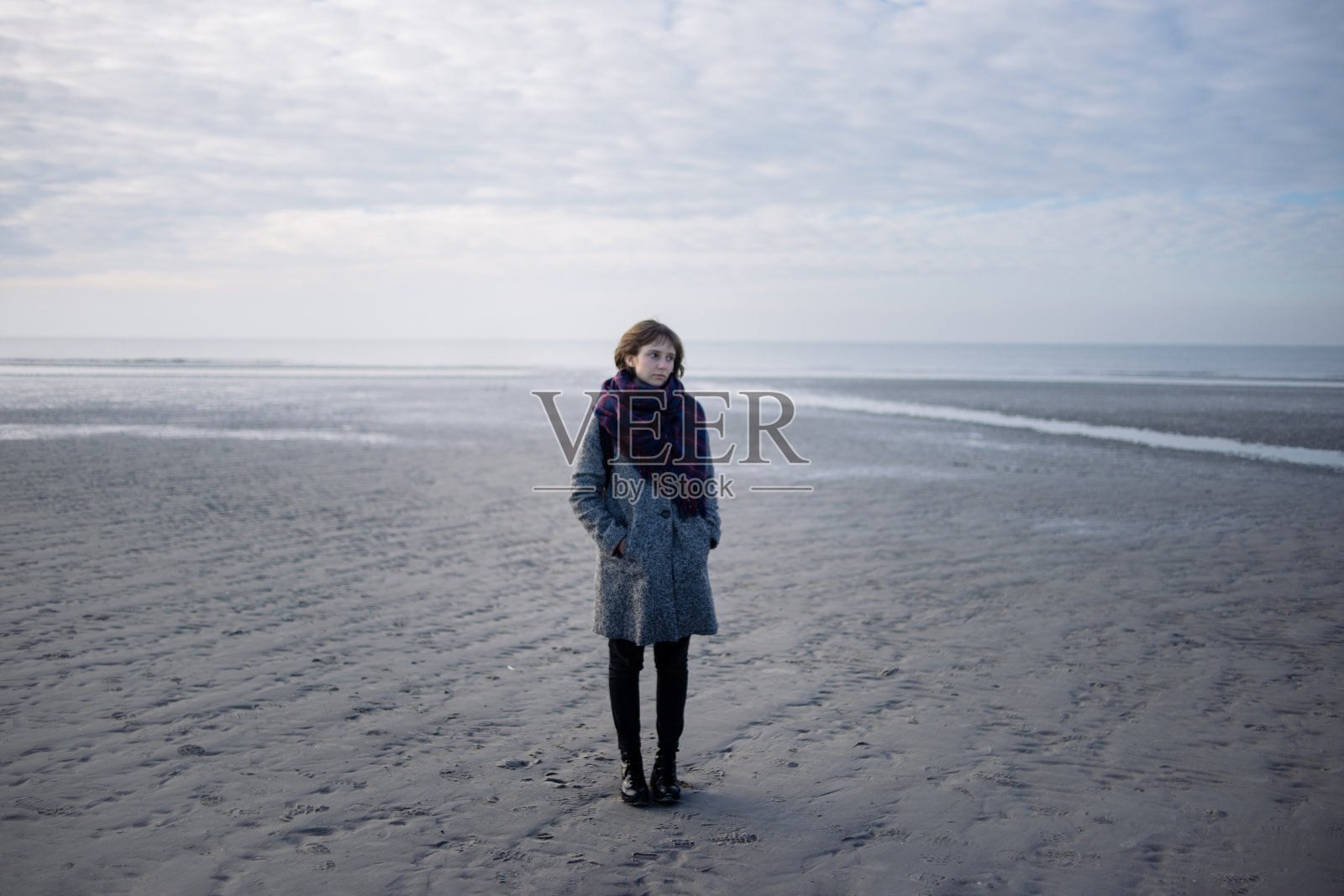 穿着大衣的年轻女子站在冬天的海滩上照片摄影图片