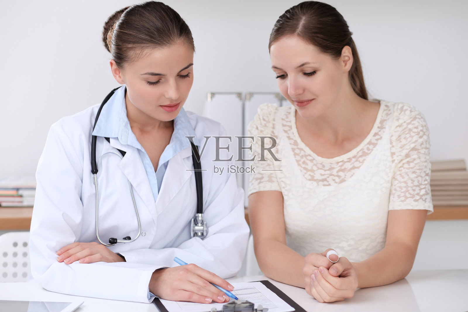 医生和病人坐在医院办公室的桌子前愉快地交谈。医疗保健理念照片摄影图片