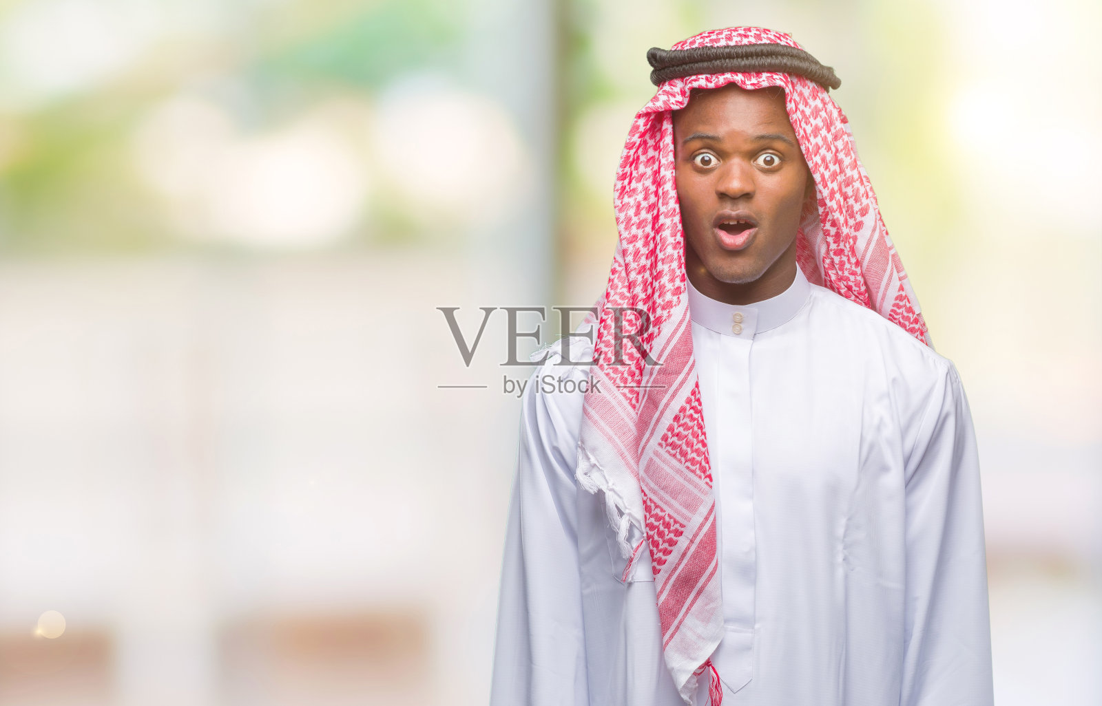 年轻的阿拉伯裔非洲人穿着传统的keffiyeh在孤立的背景害怕和震惊与惊讶的表情，恐惧和兴奋的脸。照片摄影图片