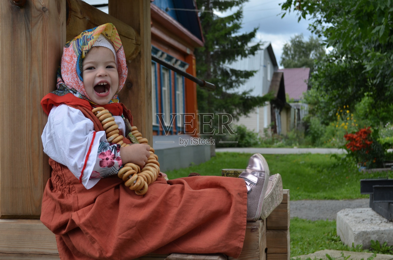 美丽的小女孩穿着民间长袍在井边吃百吉饼照片摄影图片