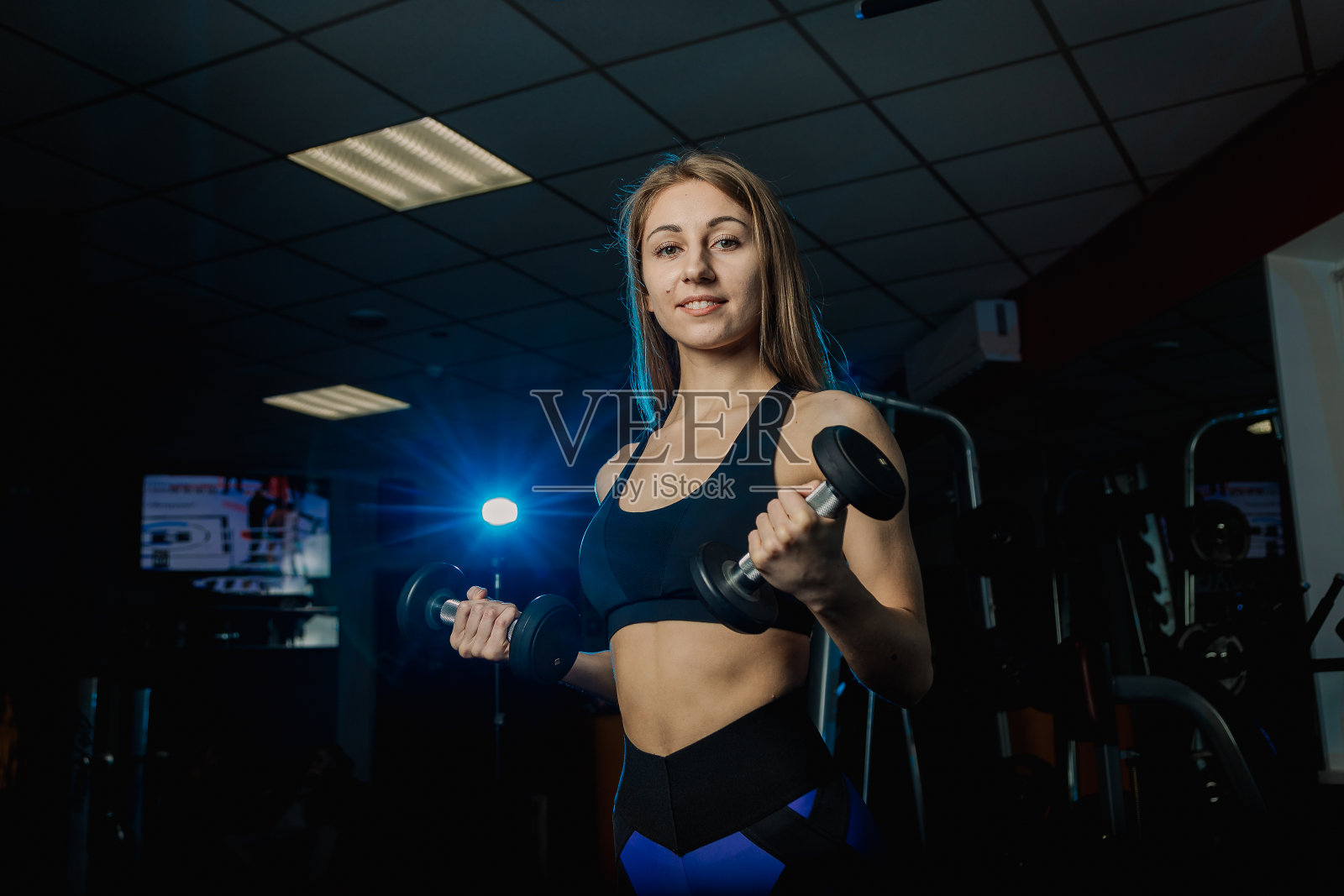 年轻漂亮的女人在健身房用哑铃锻炼。二头肌照片摄影图片