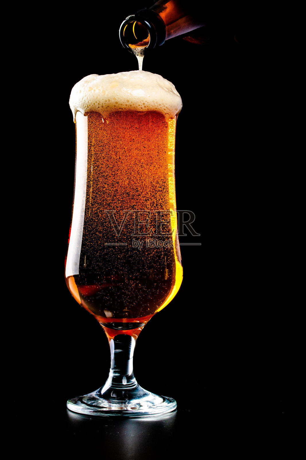 啤酒正从黑色背景的瓶子中倒入玻璃杯中照片摄影图片