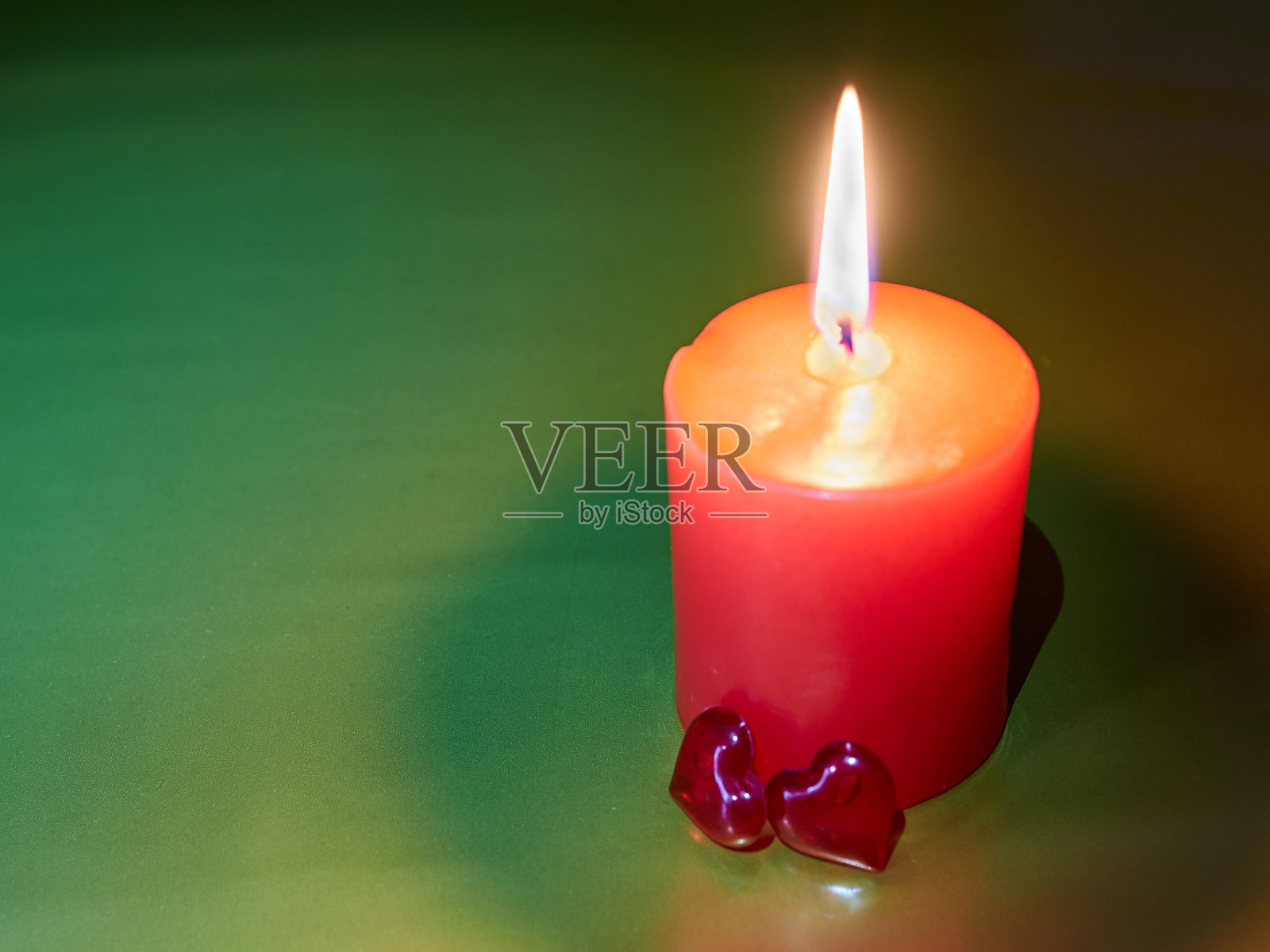 绿色装饰背景上的红色浪漫蜡烛，旁边是两颗红色的玻璃心。爱的象征。浪漫晚餐。照片摄影图片