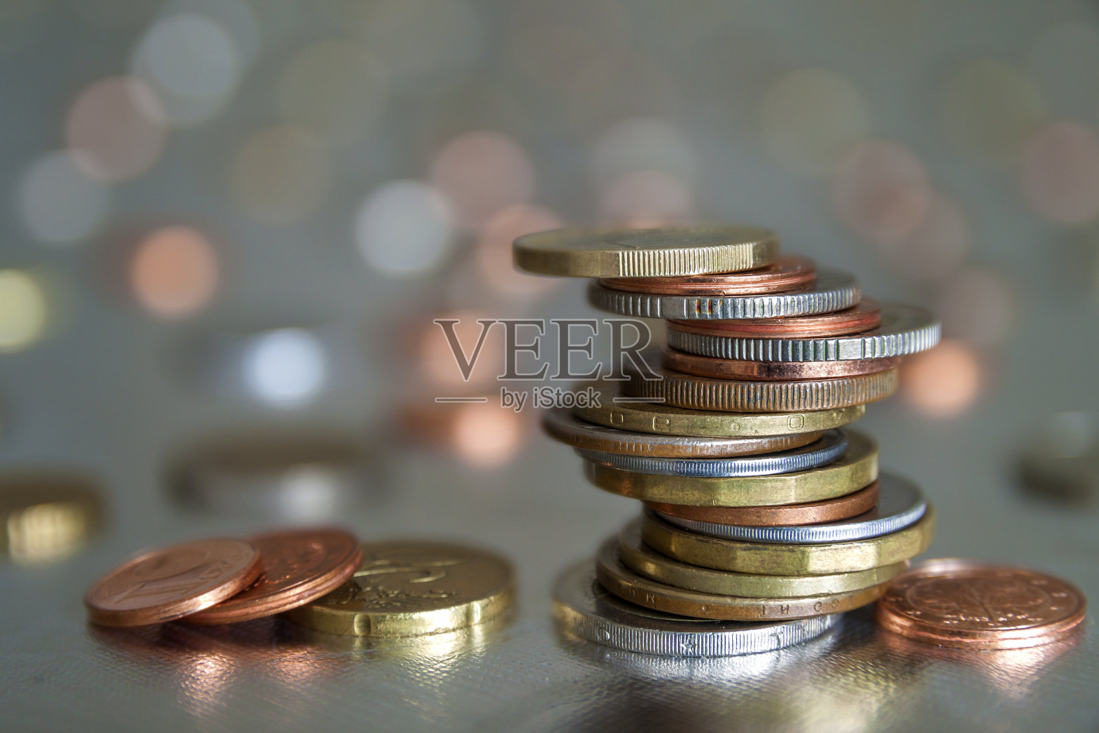 不同大小和颜色的闪亮硬币堆在彩色模糊的蓝色抽象背景上，彼此不均匀地堆叠。存钱和财务风险的概念。照片摄影图片