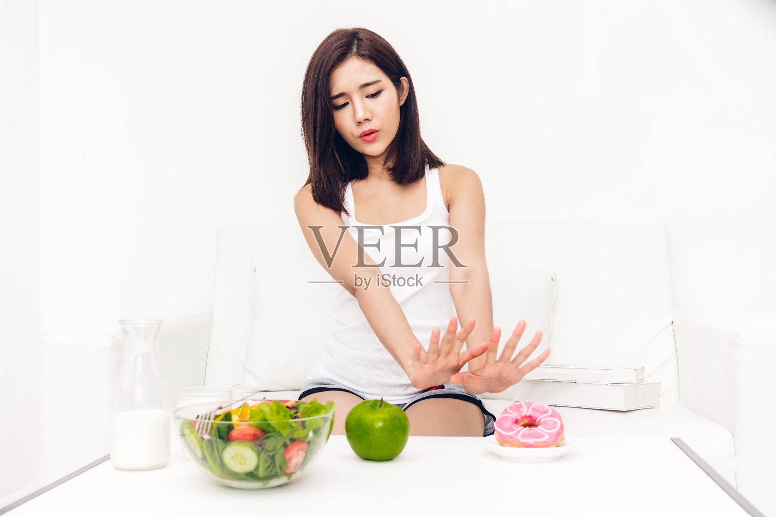 女人在健康沙拉和卡路里炸弹巧克力甜甜圈之间做出选择。女人拒绝在家里吃不健康的甜甜圈。健康饮食与垃圾食品概念照片摄影图片