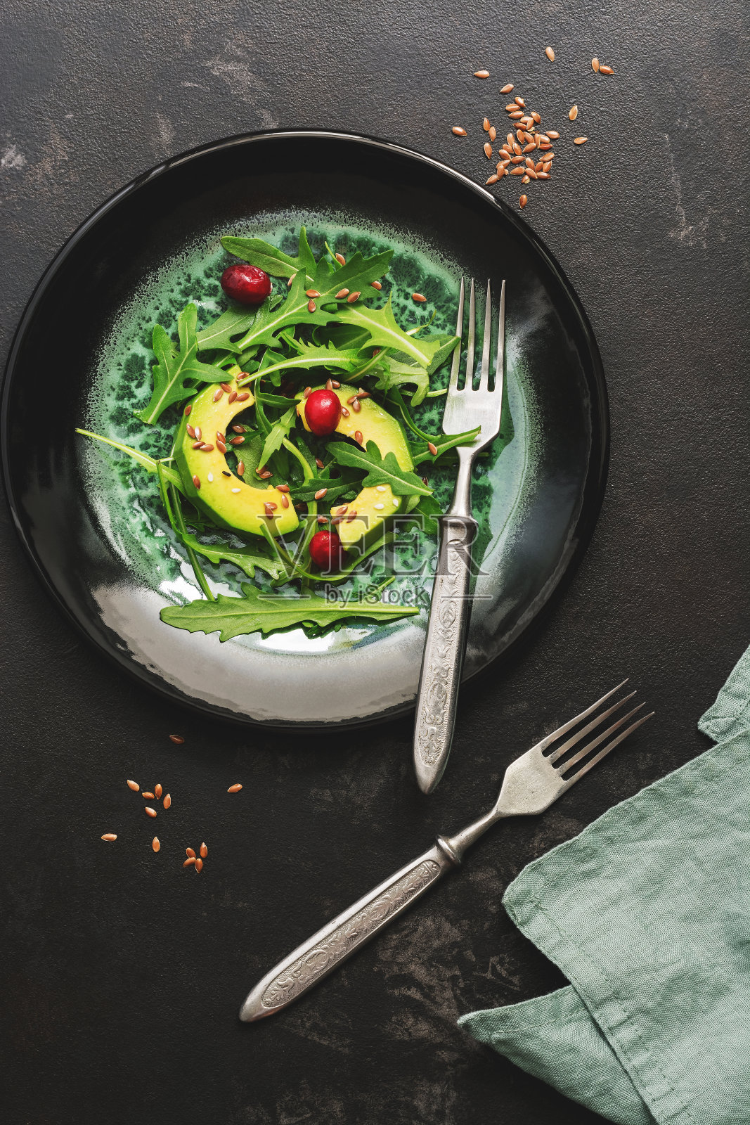 健康的素食沙拉，鳄梨，芝麻菜，荚蒾种子和浆果，黑色的石头背景。前视图。照片摄影图片