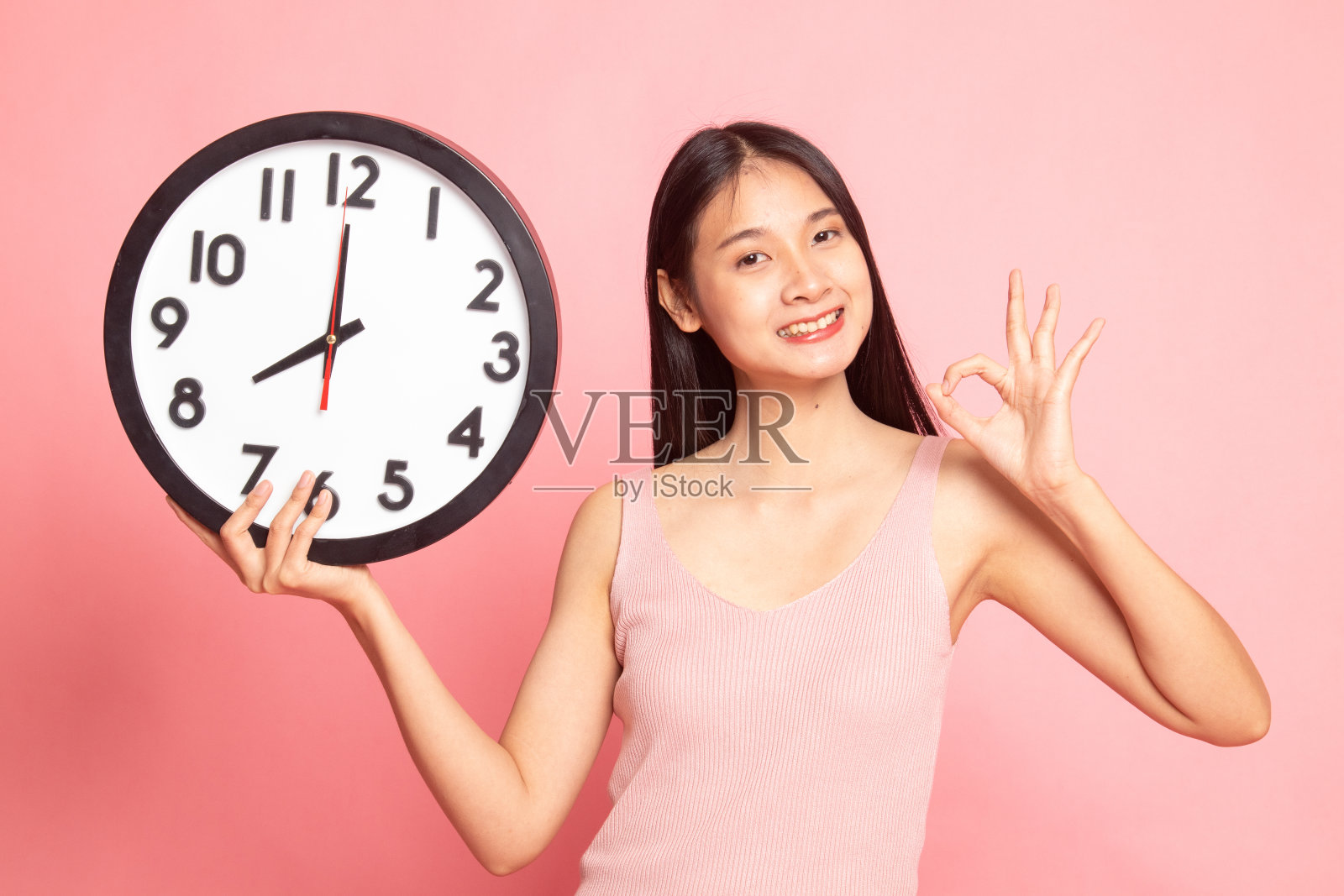 年轻的亚洲女子用时钟显示OK。照片摄影图片