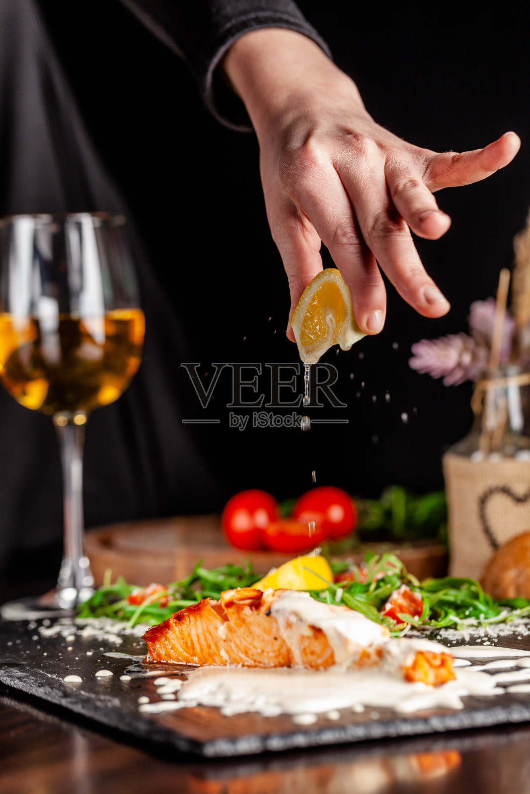 意大利菜的概念。三文鱼片配芝麻菜、圣女果和帕尔玛芝士配奶油柠檬汁。桌上有一杯白葡萄酒。餐厅里的菜。照片摄影图片