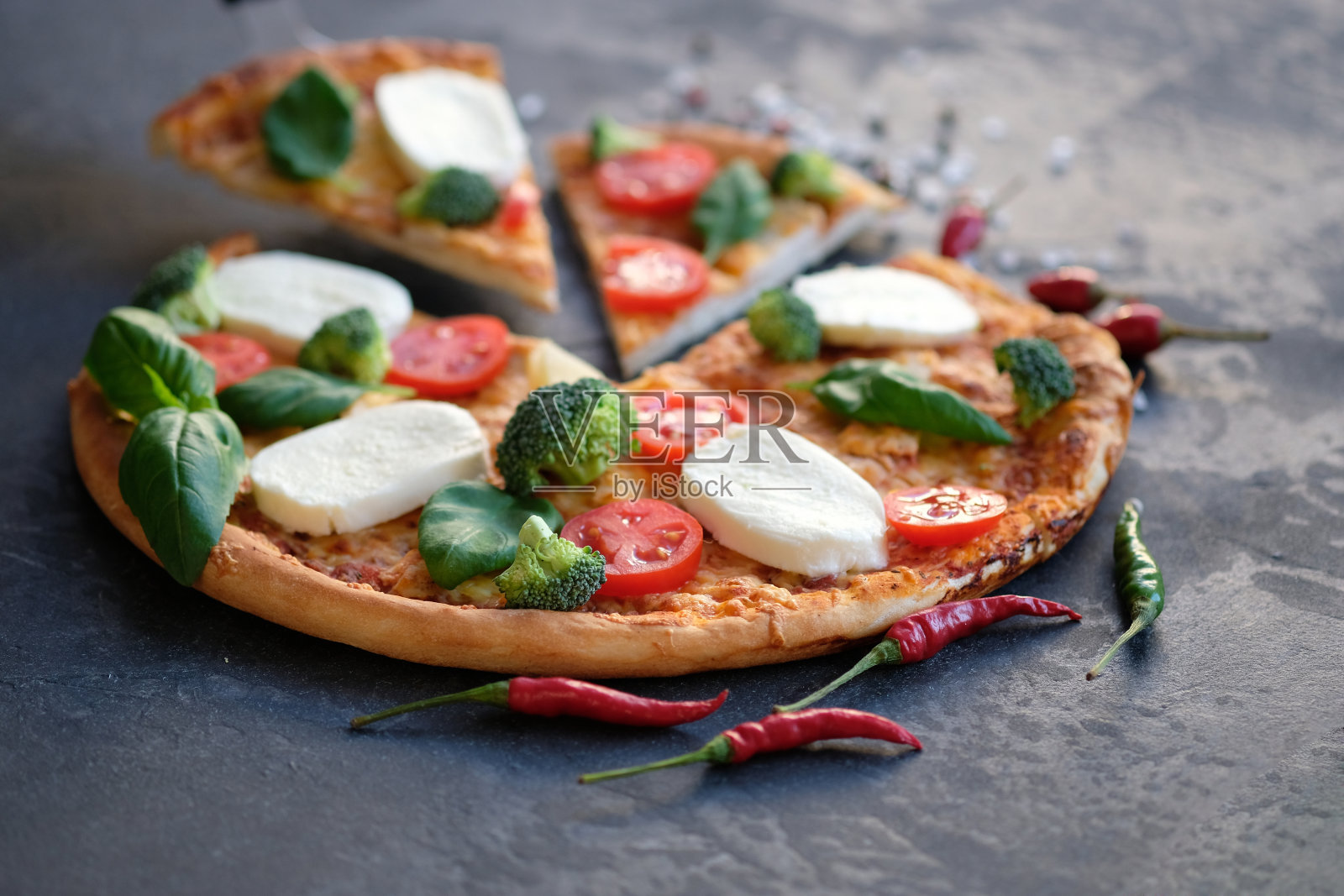 切片披萨配马苏里拉奶酪，西红柿，西兰花，香料和新鲜罗勒。意大利披萨。黑色石头背景上的披萨照片摄影图片