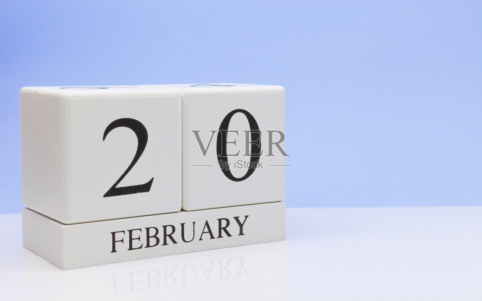 2月的认识。月20日，日历在白色的桌子上用反光，以浅蓝色为背景。冬天的时候，空白的文字照片摄影图片