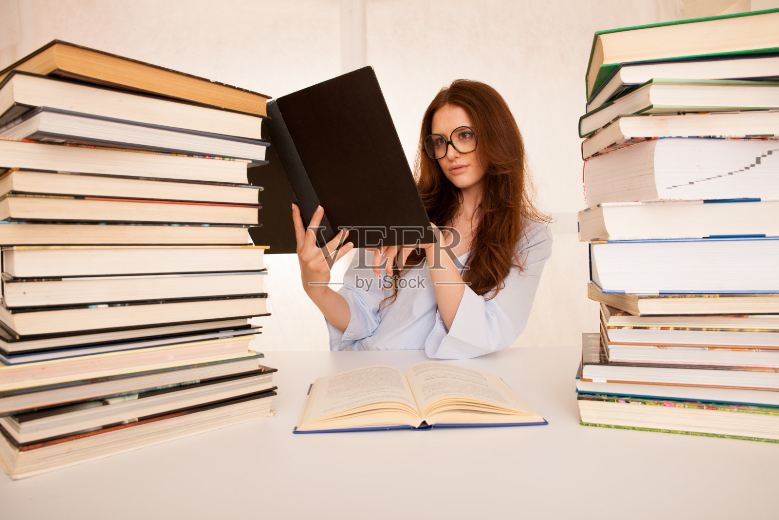 迷人的年轻女子研究成堆的书在她的书桌上照片摄影图片