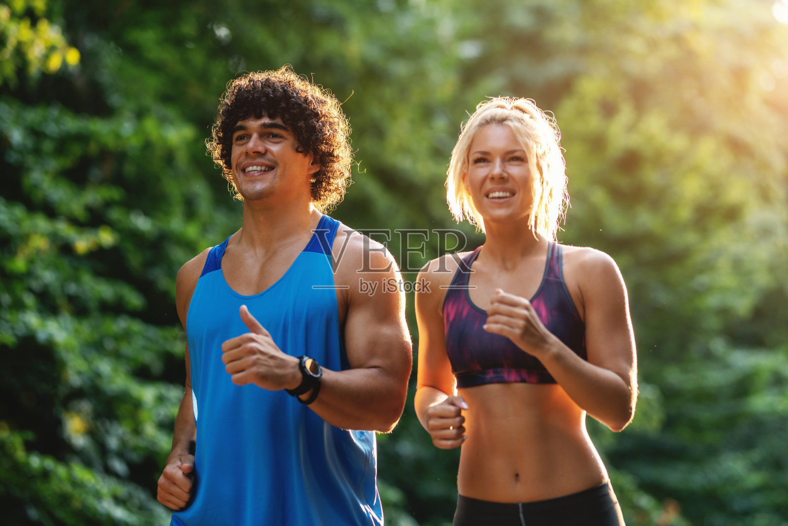 在阳光明媚的夏日，一对专注的微笑情侣在森林里奔跑。腰。照片摄影图片