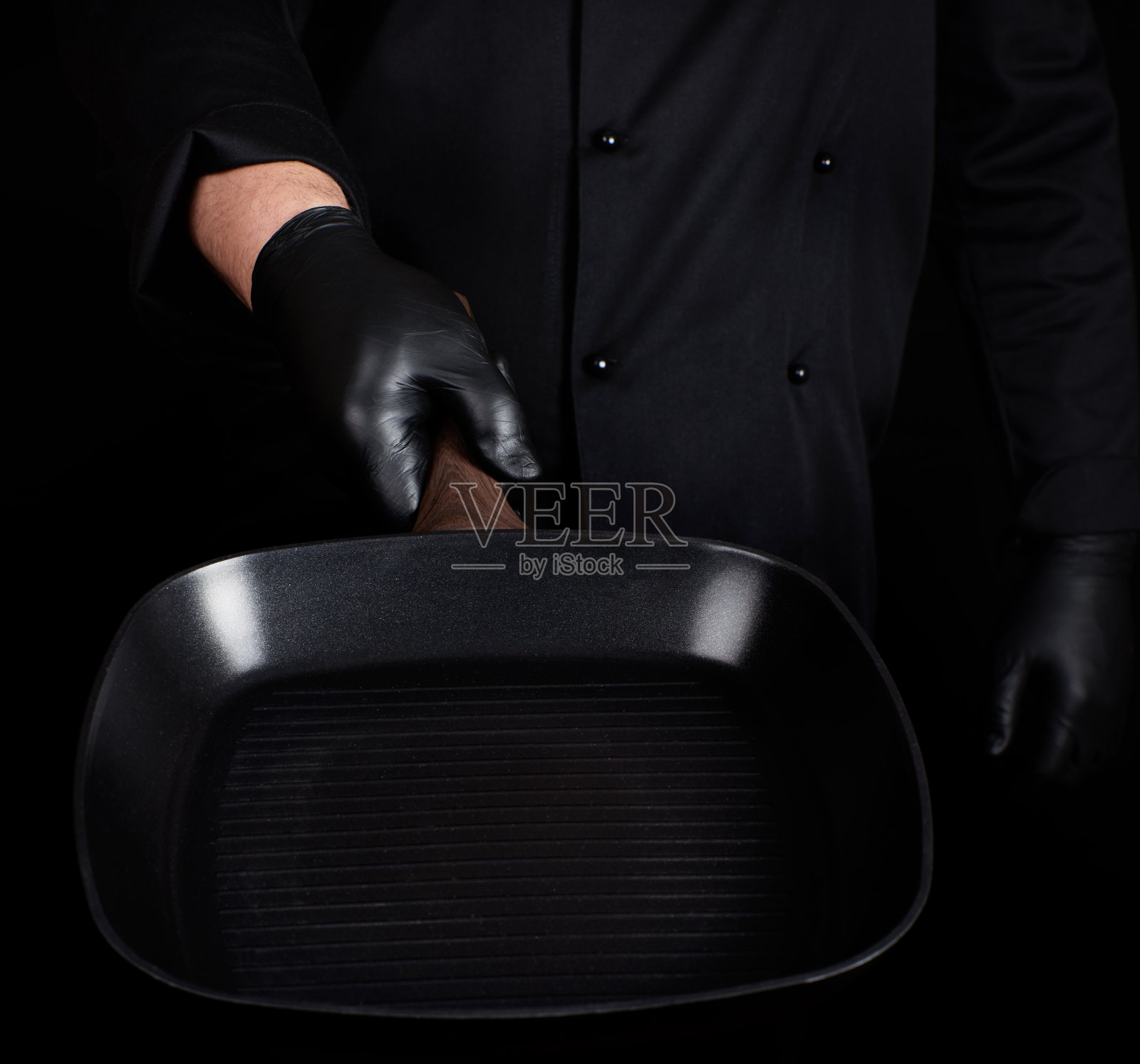 厨师穿着黑色制服，戴着黑色乳胶手套，拿着一个空的方形烤盘照片摄影图片