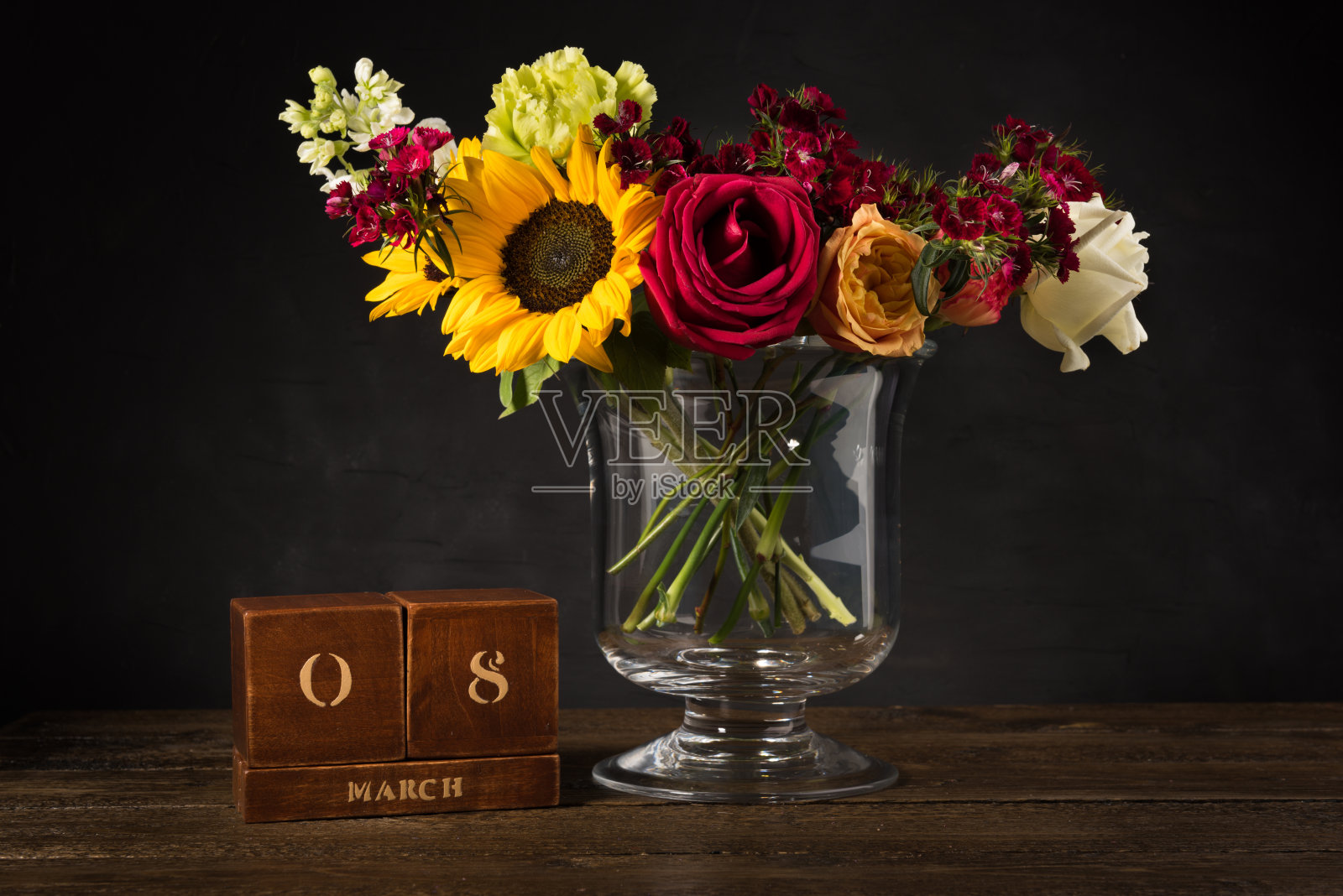 一束白色、黄色和红色的花，插在一个花瓶上，背景是黑色的。国际Womenâ日古董木万年历为3月8日在黑色的背景。照片摄影图片