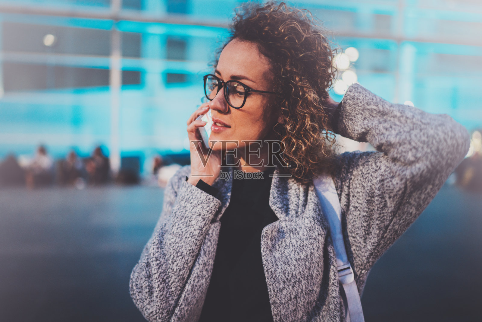 微笑的年轻女孩用她的手机打电话，而站在晚上的街道上。模糊背景上的散景和闪光效果。照片摄影图片