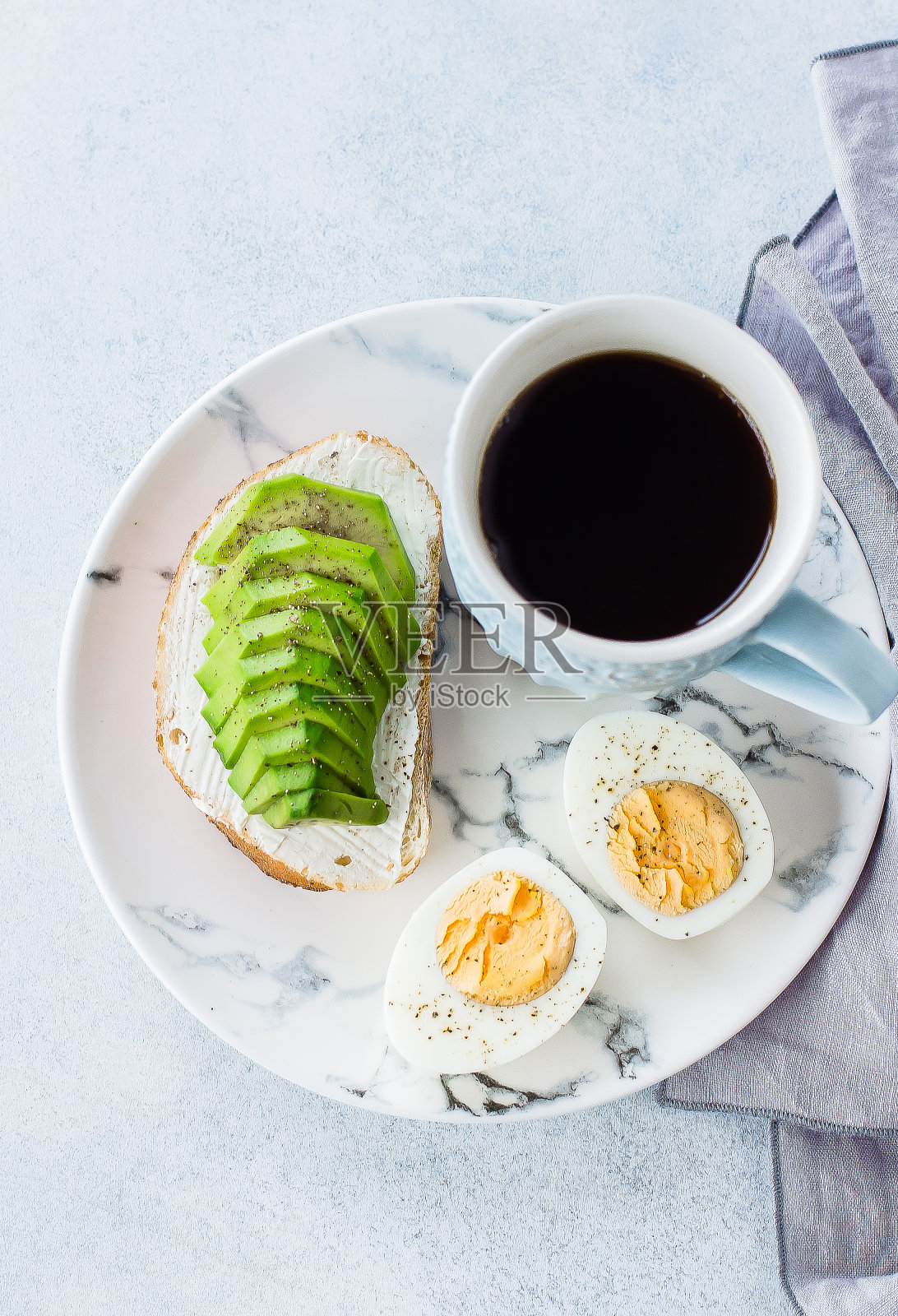 俯视图的健康素食早餐概念。全谷物面包三明治，鳄梨，煮鸡蛋和一杯黑咖啡放在蓝色的桌子上。干净的吃。照片摄影图片