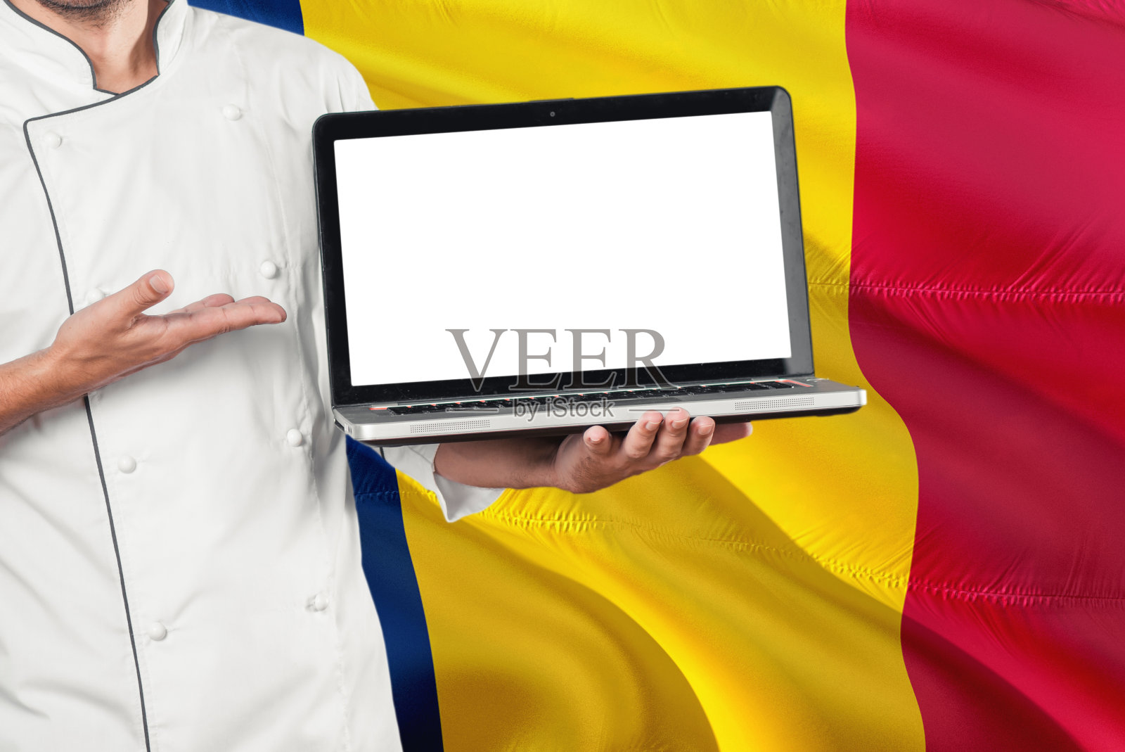乍得厨师拿着笔记本电脑与空白屏幕上的乍得国旗背景。库克穿着制服，指着笔记本电脑找拷贝空间。照片摄影图片