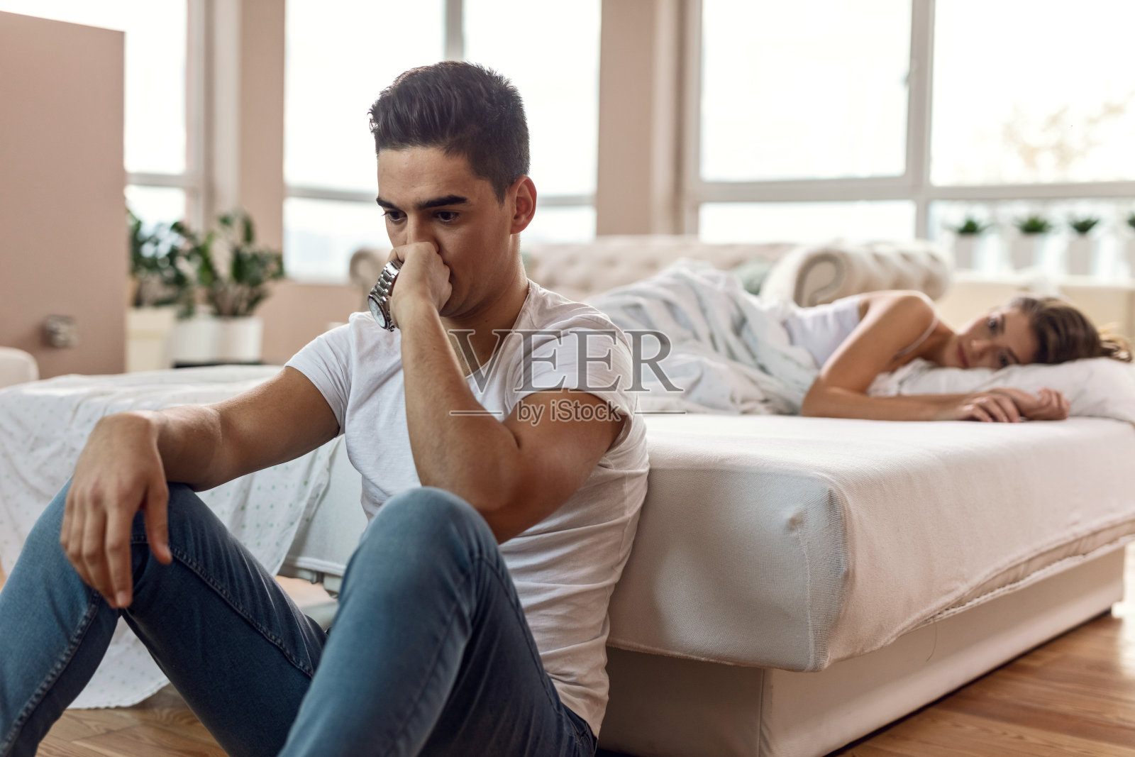 年轻男子感到悲伤，而有问题，他的女朋友在卧室。照片摄影图片