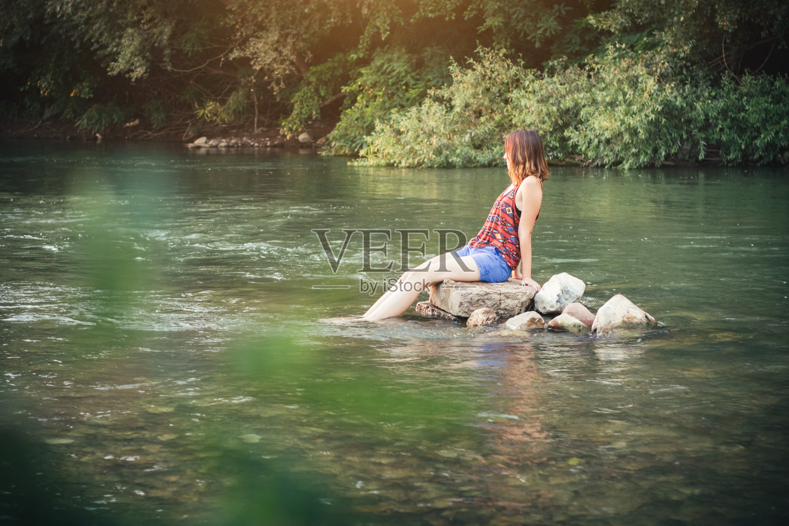 女孩坐在河里的一块石头上照片摄影图片